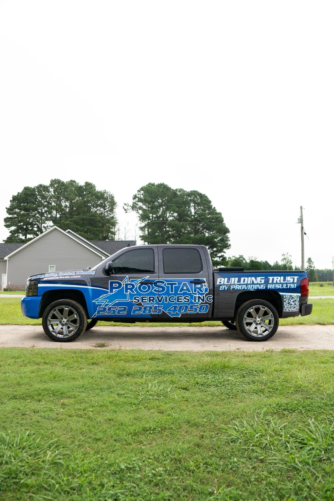Blue and black pickup truck with custom graphics parked on a gravel drive in front of a house.