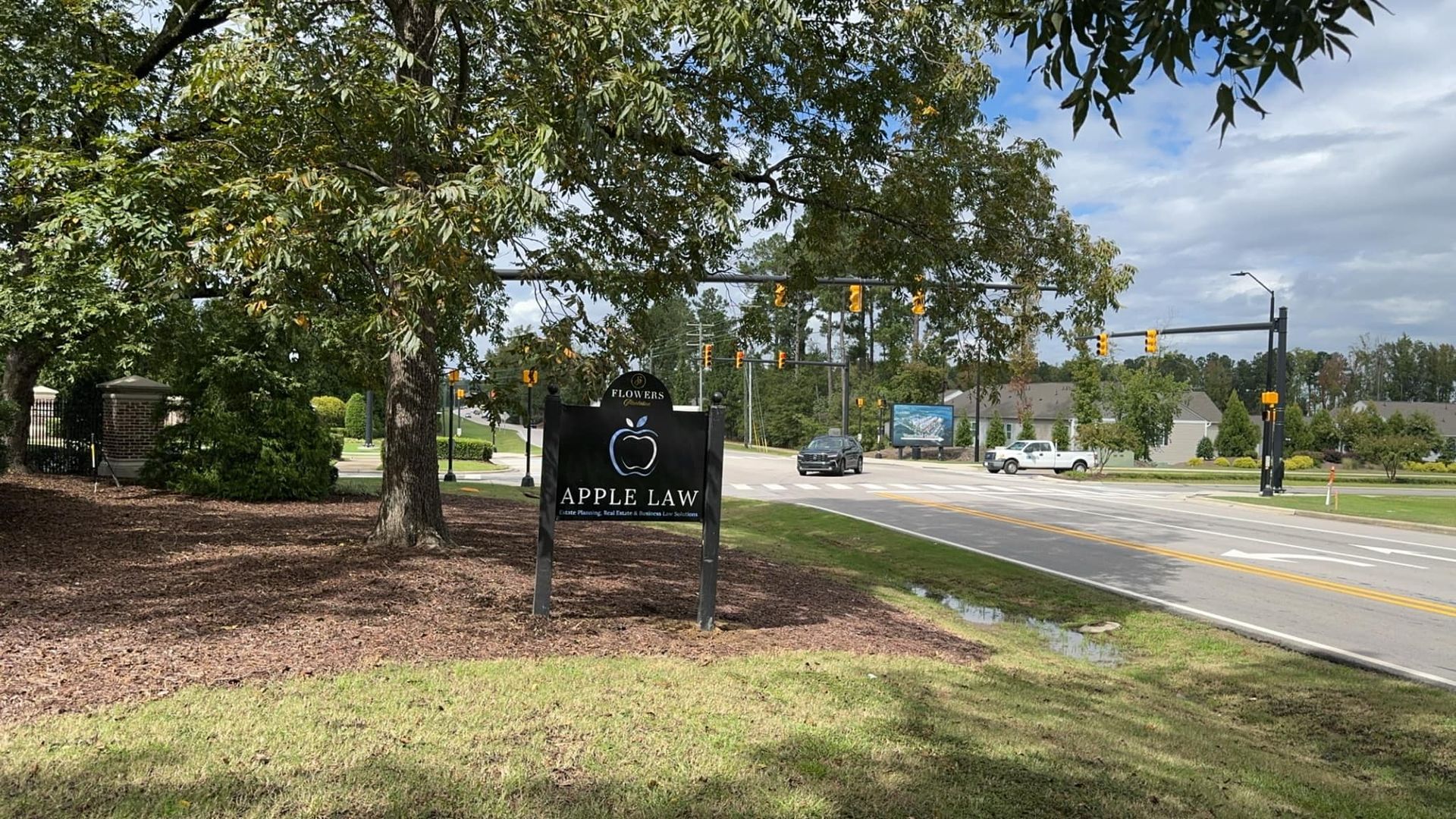 Sign for Apple Lane at a road intersection, trees overhead, cloudy sky.
