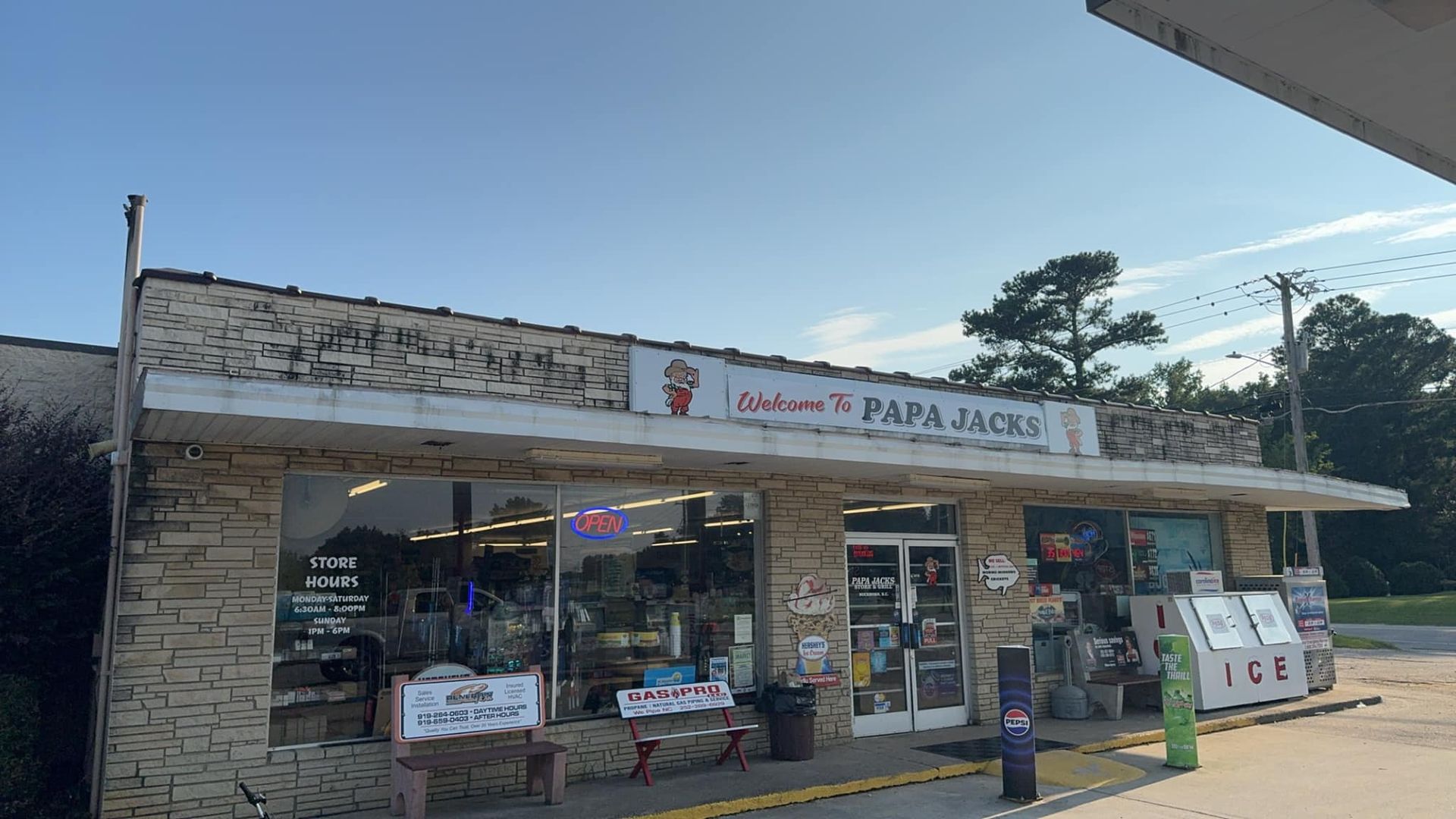 Exterior of Cajun's Papa Jacks store, a convenience store under a blue sky, with gas pumps and ice machine.