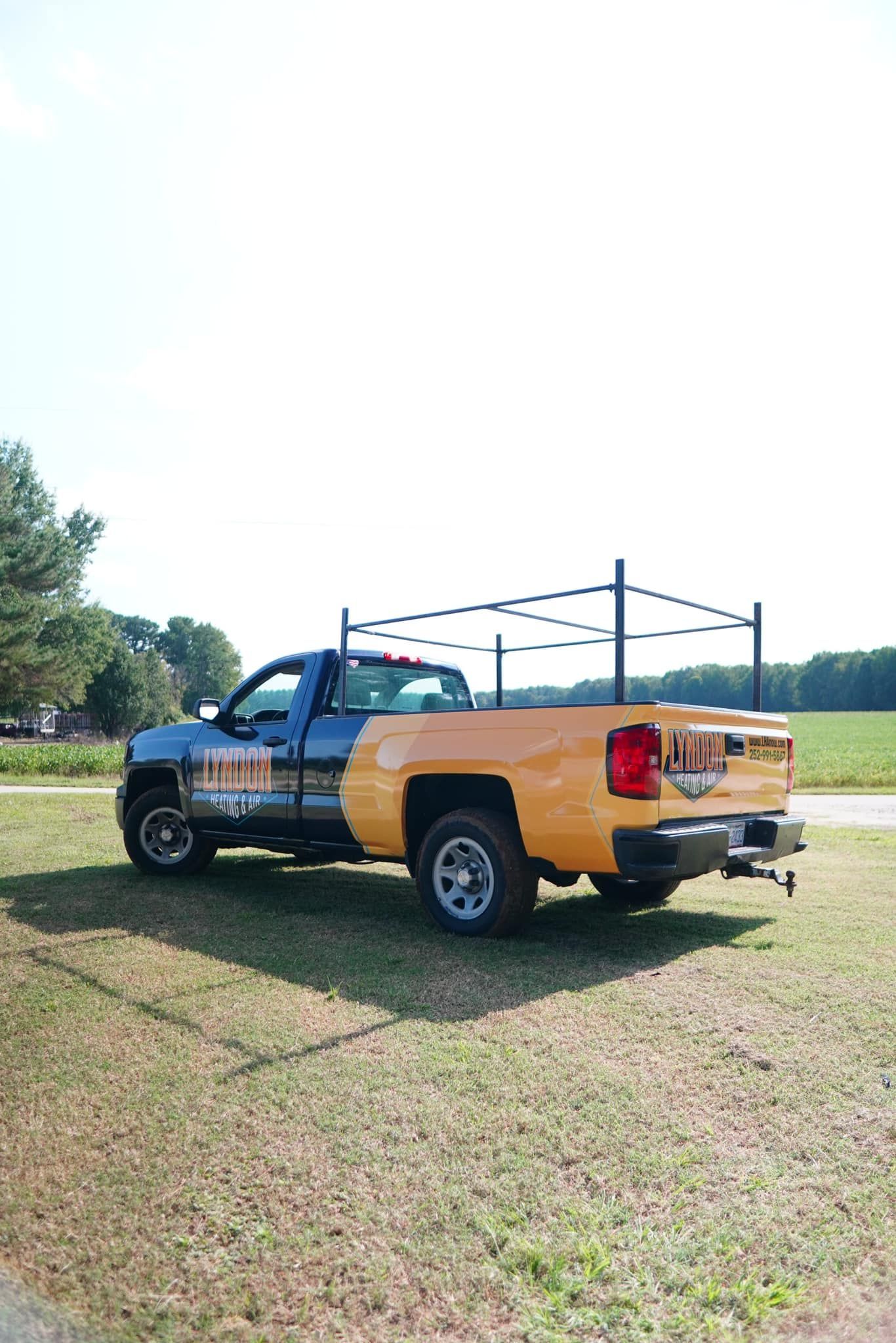 Blue and yellow pickup truck with ladder rack parked on grass field.
