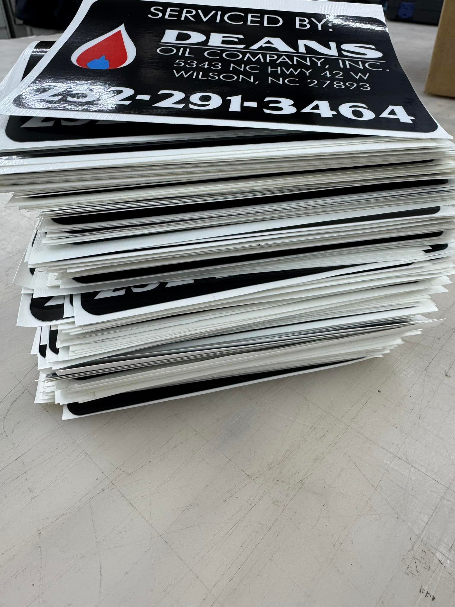 Stack of black and white Dean's Oil Company signs on a light-colored surface.