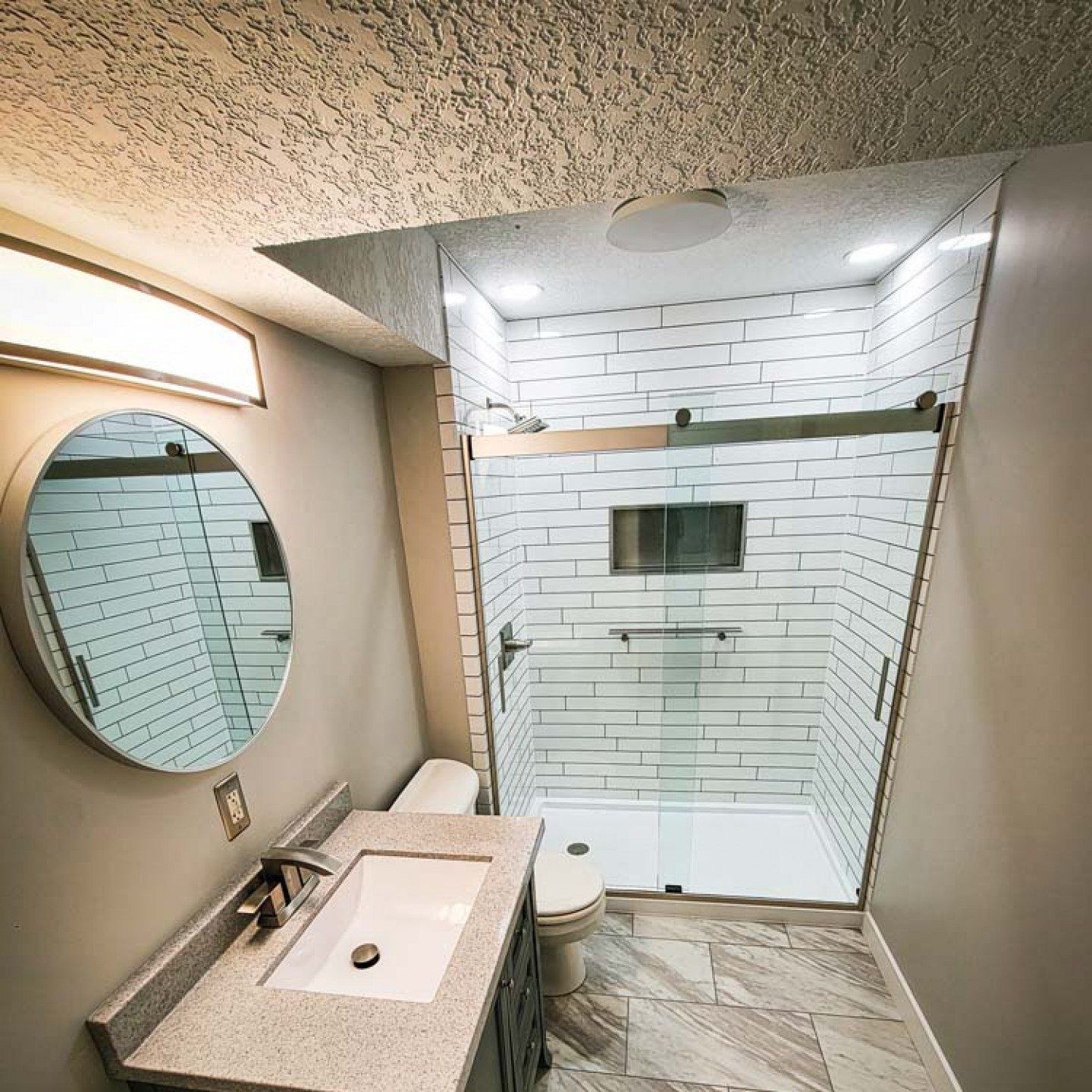 Modern bathroom with vanity, round mirror, and glass shower enclosure in white and beige tones