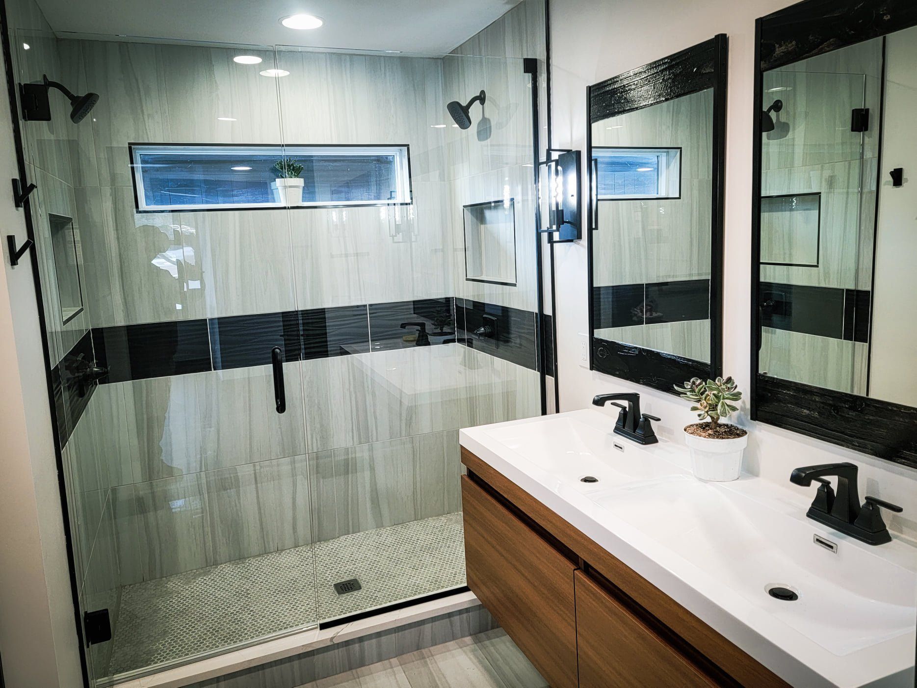Modern bathroom with glass shower, black-framed mirrors, and white vanity with wood cabinet accents