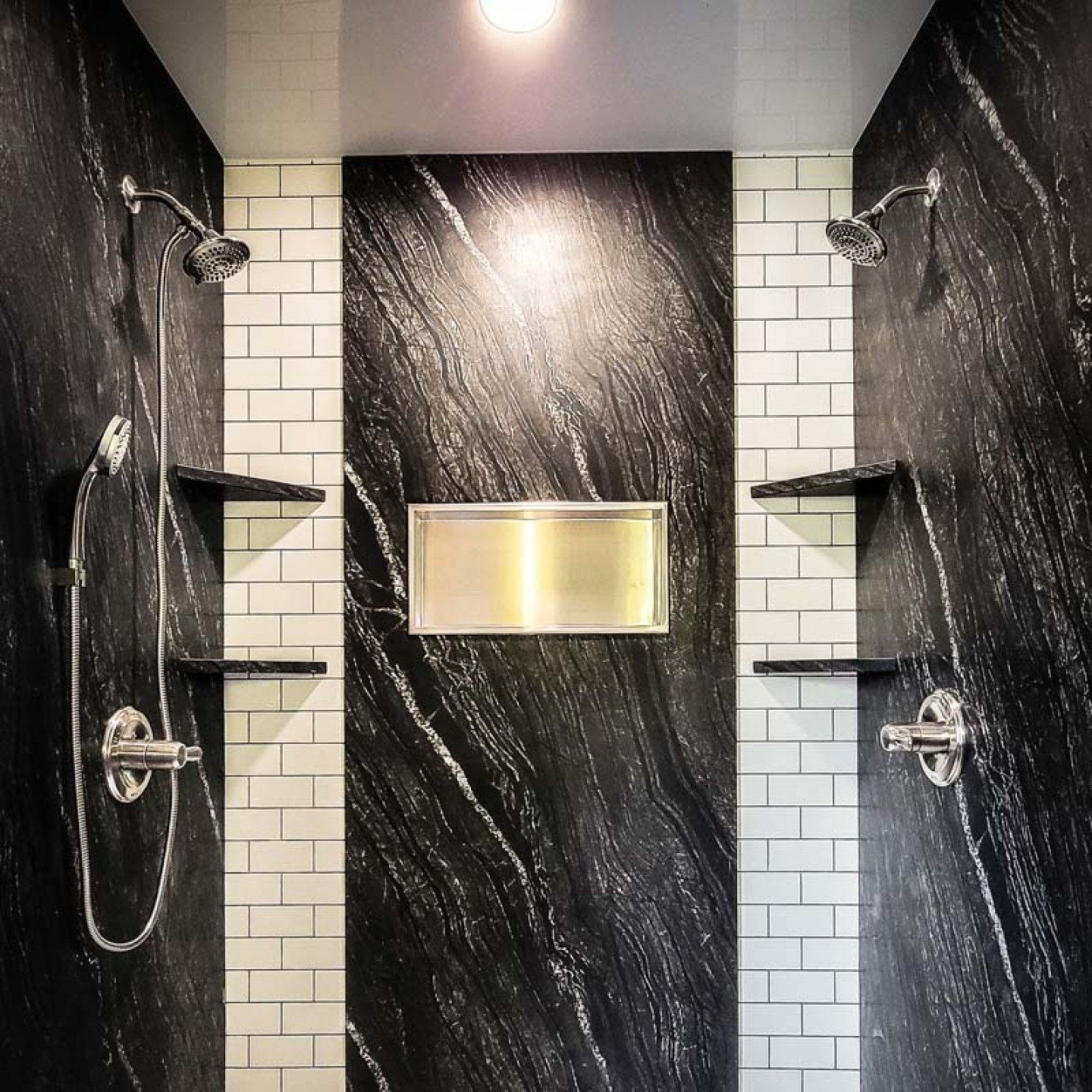 Modern shower with black marble walls, white tile accents, dual showerheads, and built-in shelves.