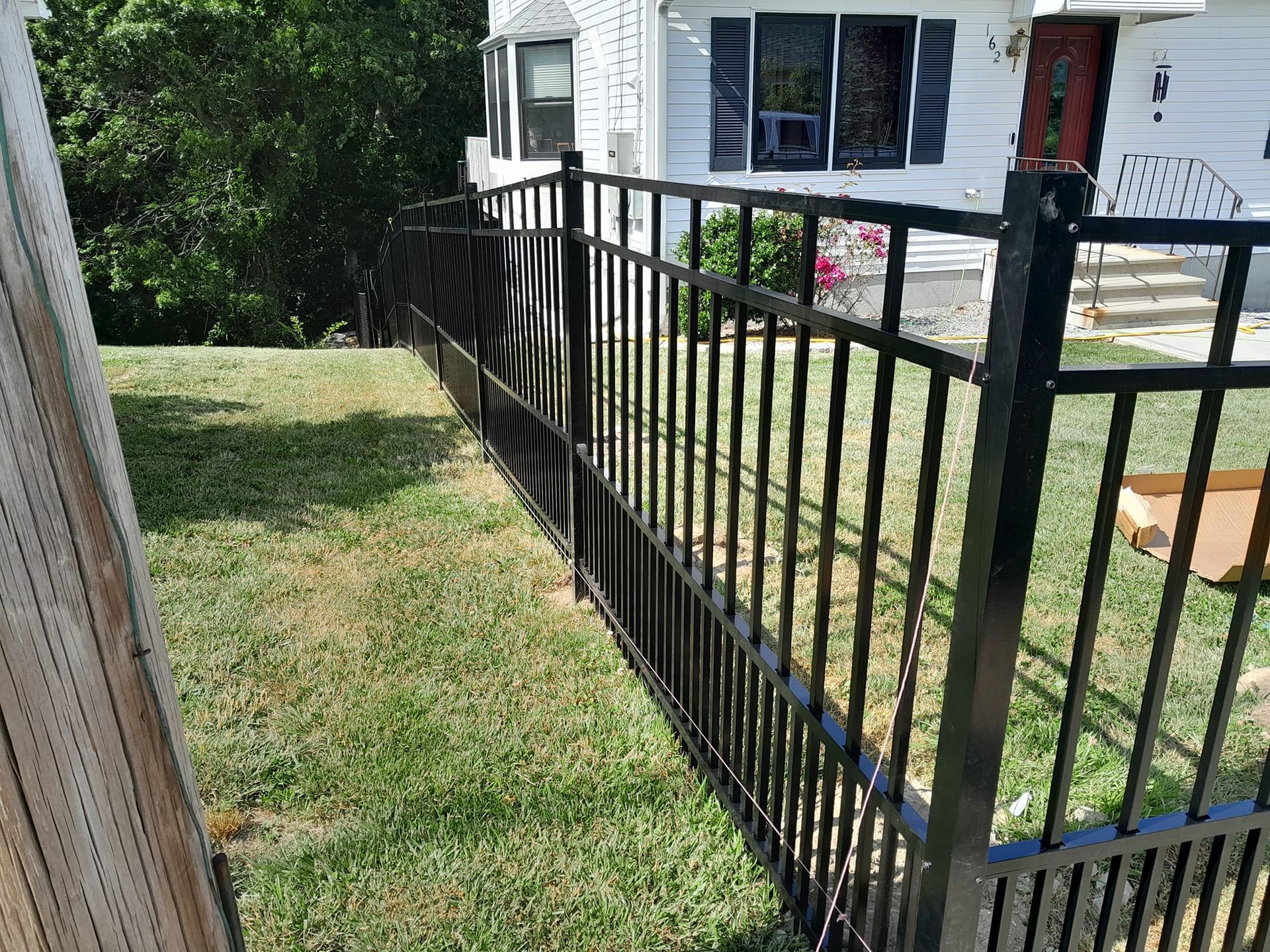 A black fence surrounds a lush green yard in front of a white house.