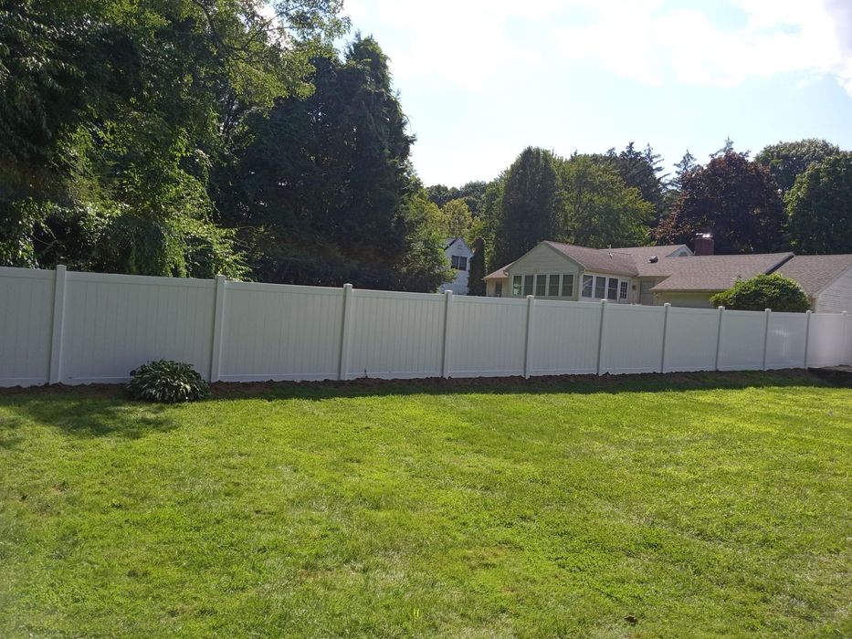 A white fence surrounds a lush green yard with houses in the background.