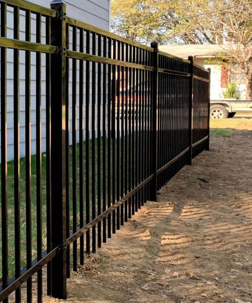 A black metal fence surrounds a dirt path in front of a house.