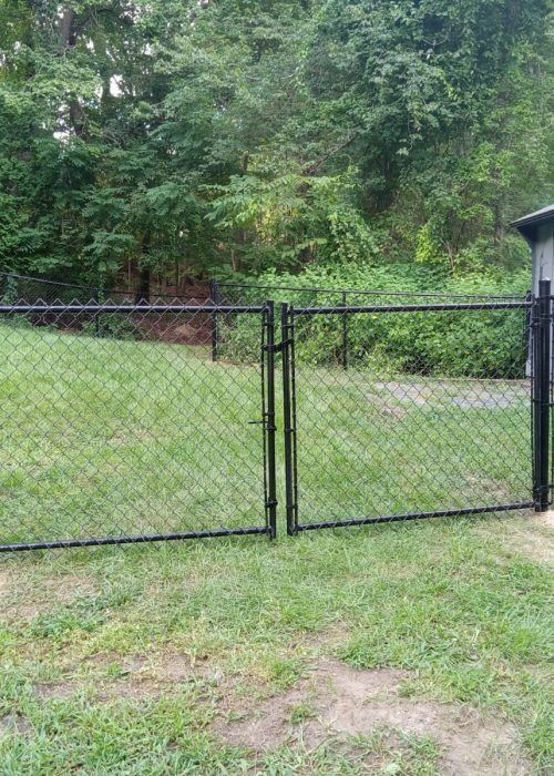 A chain link fence with a gate in the middle of a lush green field.