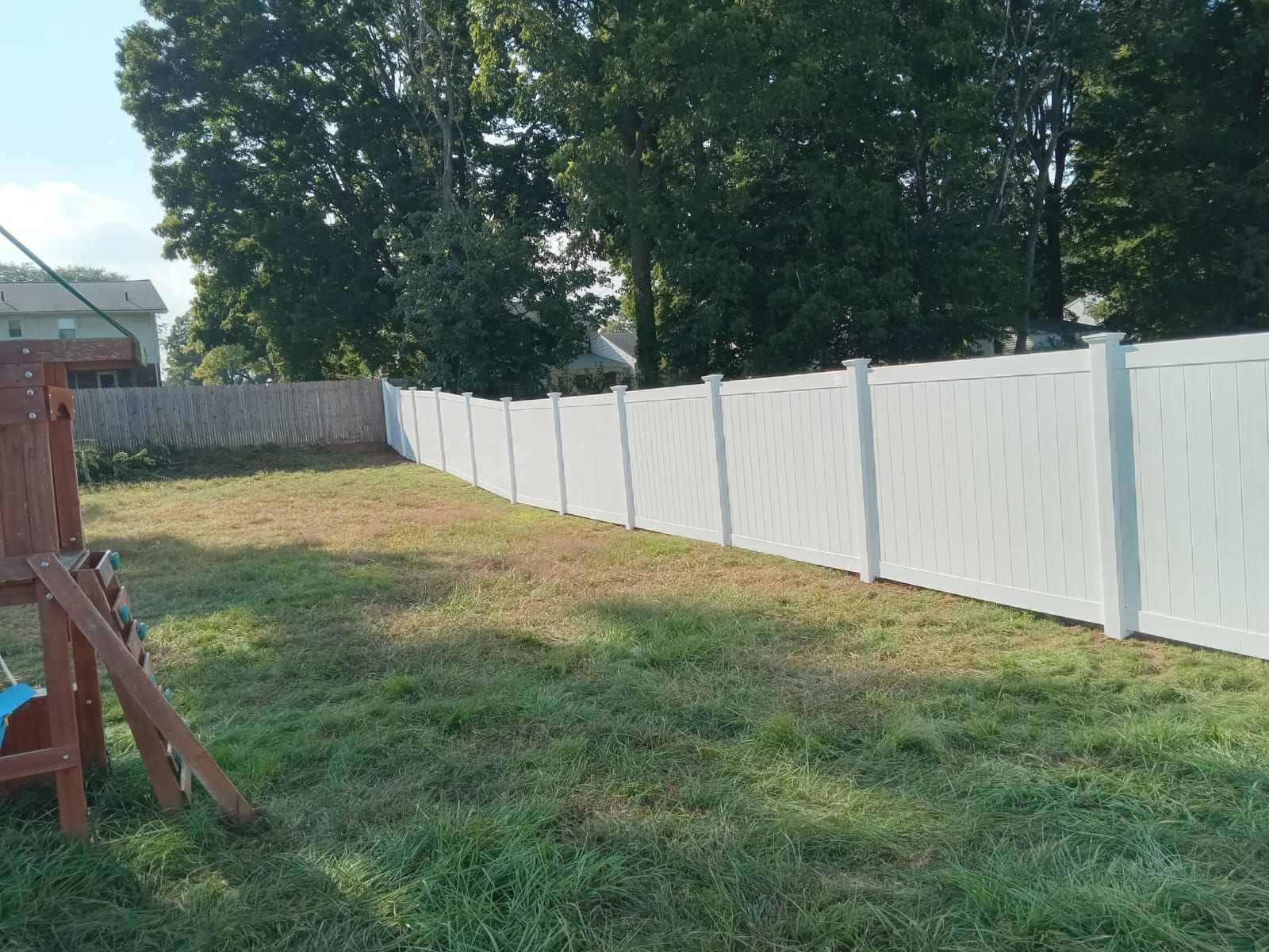 A white fence surrounds a lush green yard with a swing set in the background.