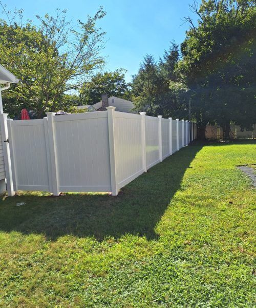 A white vinyl fence surrounds a lush green yard.