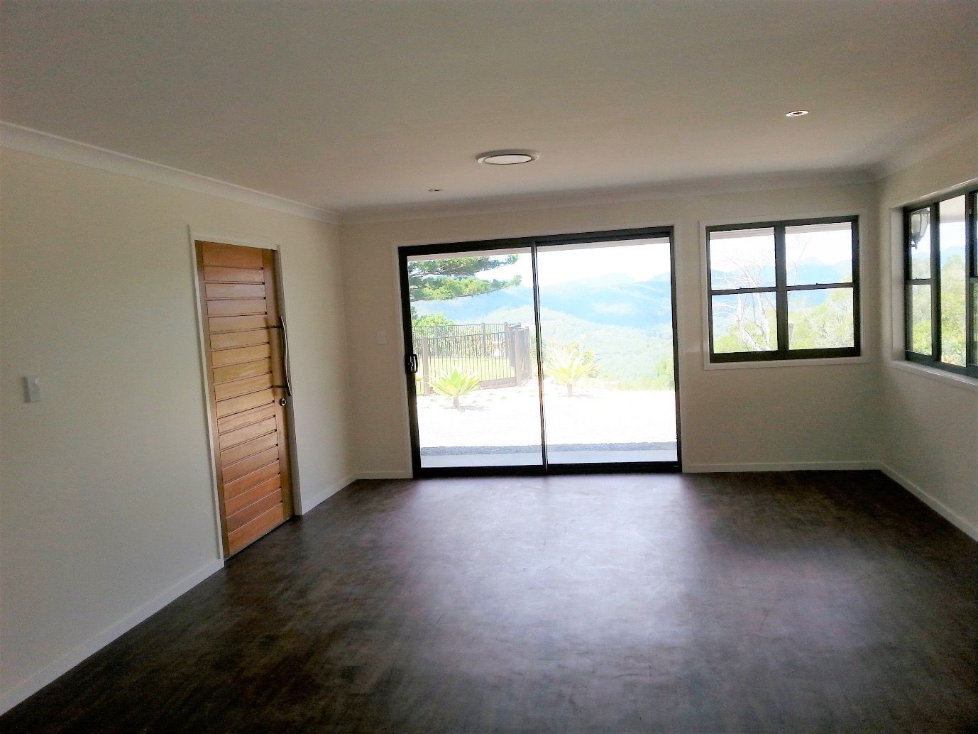 An Empty Living Room With Sliding Glass Doors and a Wooden Door  — Scott Graham Building Services In Bilambil Heights, NSW 