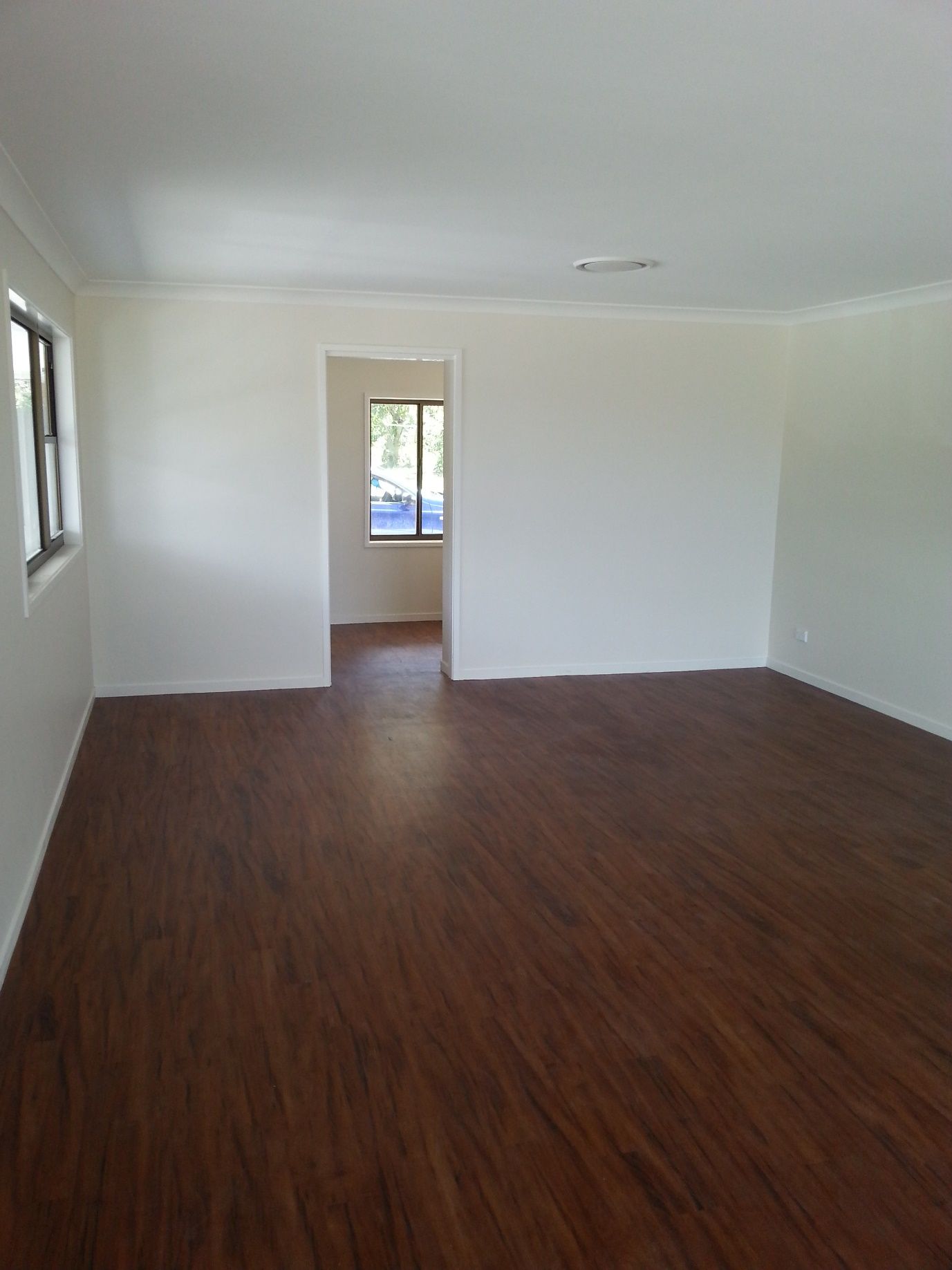An Empty Living Room With Hardwood Floors and White Walls  — Scott Graham Building Services In Bilambil Heights, NSW 