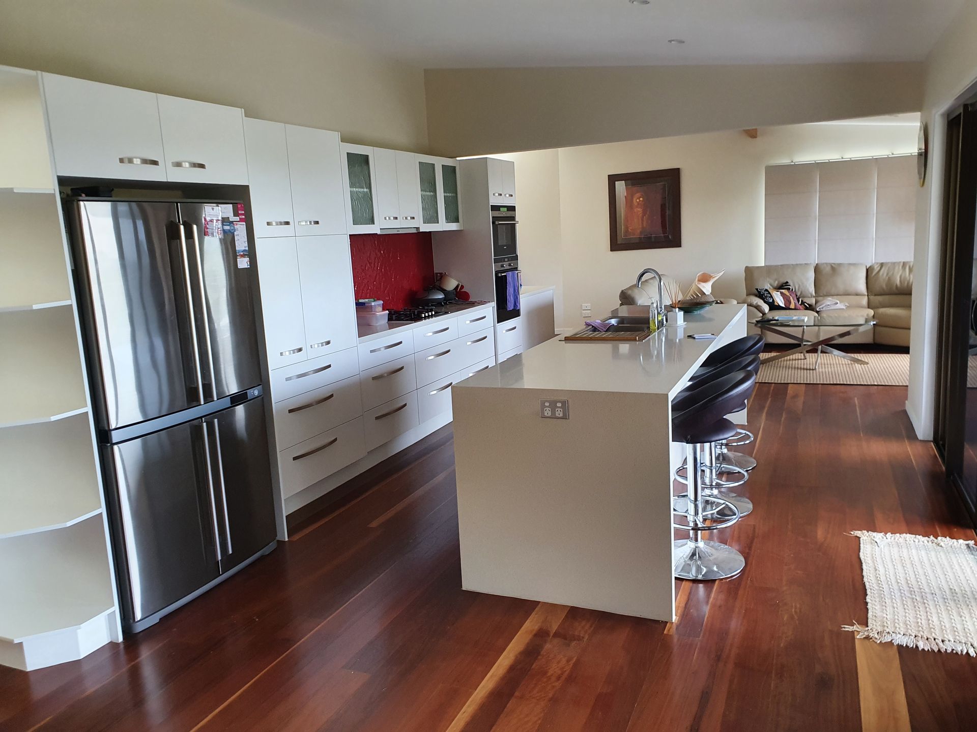 Modern kitchen with white cabinets, stainless steel fridge, island with stools, and hardwood floors.