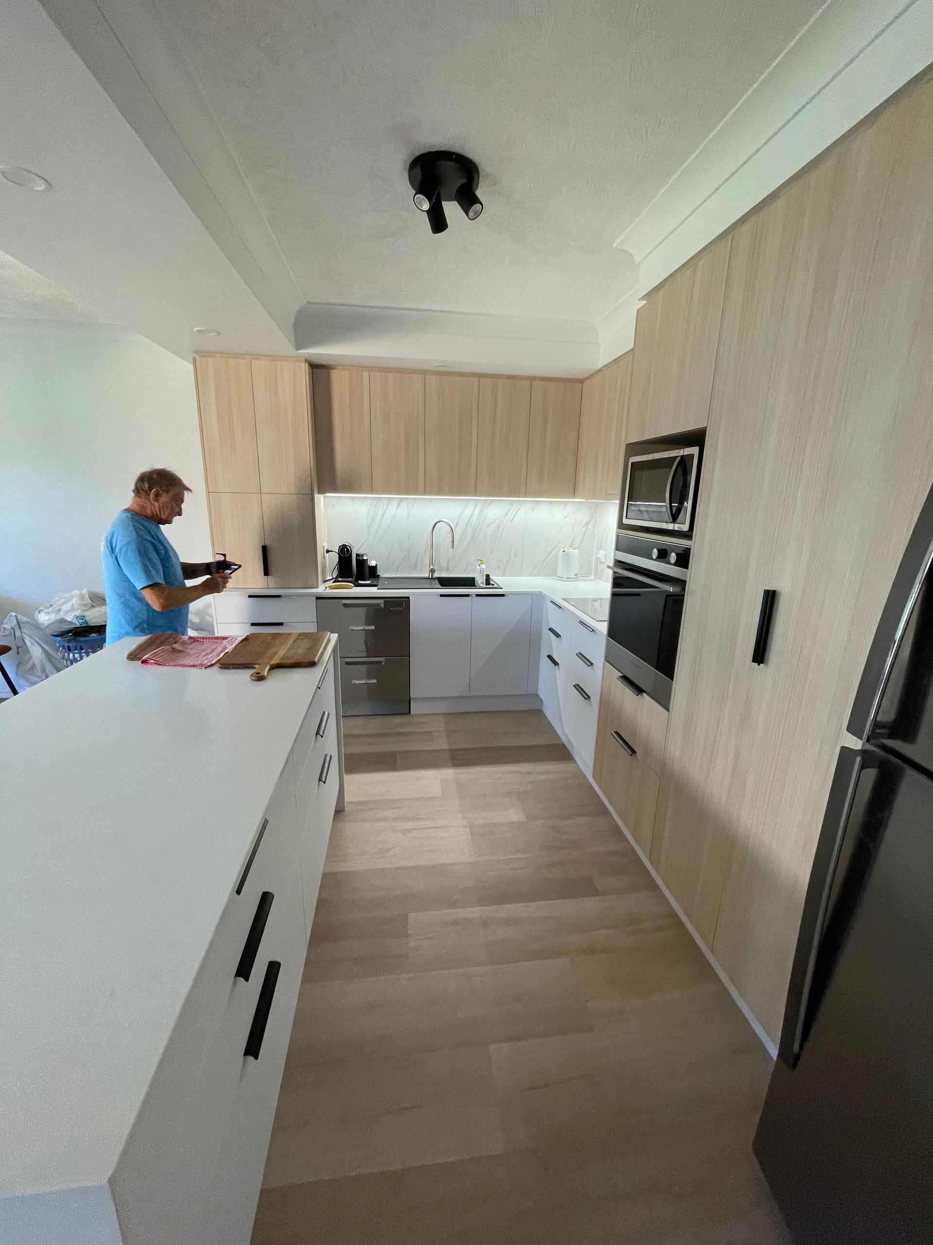A Man is Standing in a Kitchen Looking at a Tablet  — Scott Graham Building Services In Bilambil Heights, NSW