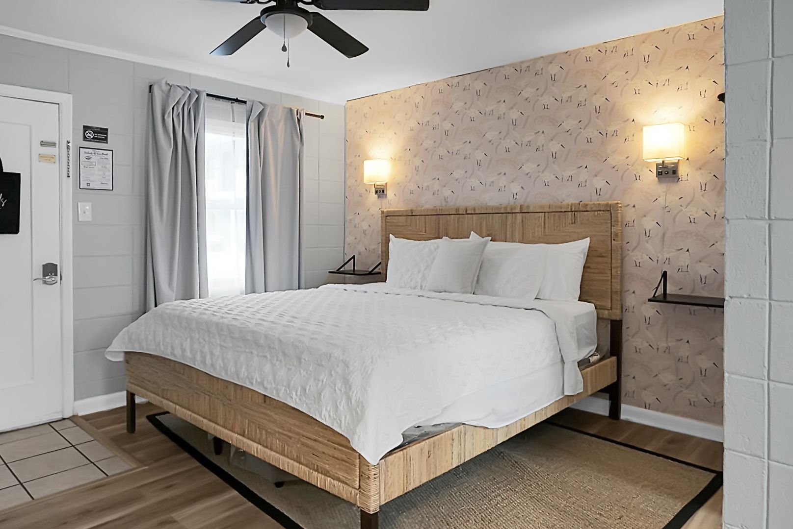 A stylish, modern room at Seabirds Motel at Kure Beach featuring a rattan bed frame, a mounted flat-screen TV, and simple furnishings. The bright and open space is ideal for a relaxing, pet-friendly stay in North Carolina.