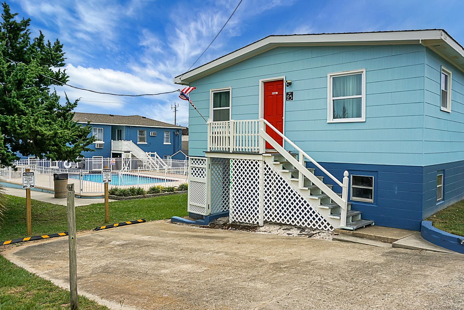 A modern guest room at Seabirds Motel at Kure Beach with a king-size bed, white bedding, a rattan bed frame, a ceiling fan, and coastal-themed wallpaper. This room offers a comfortable, pet-friendly North Carolina lodging experience.