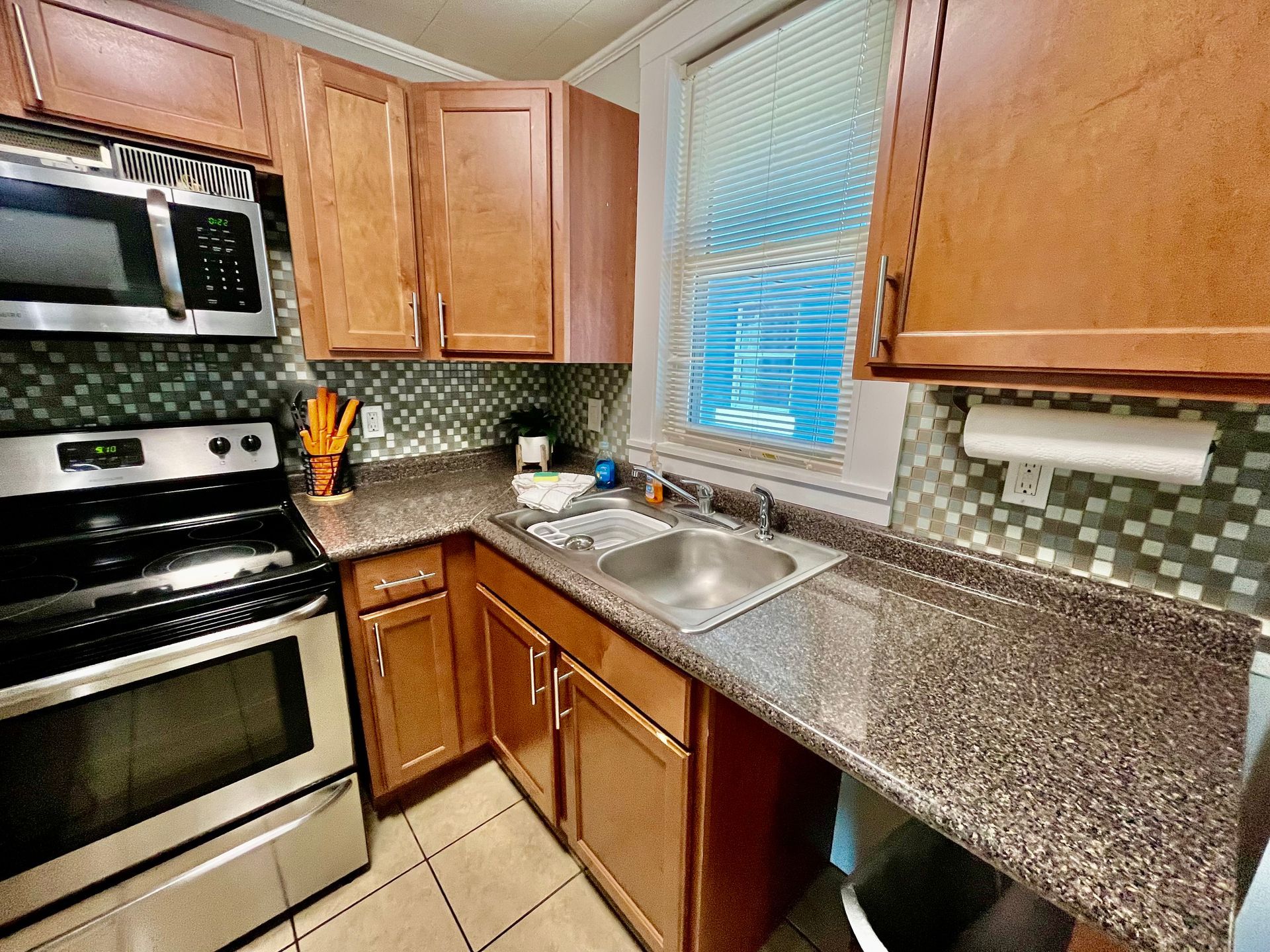 A compact kitchen at Seabirds Motel at Kure Beach featuring granite countertops, a dual sink, and stainless steel appliances. This well-appointed kitchen provides all the amenities needed for a convenient, pet-friendly stay in North Carolina.