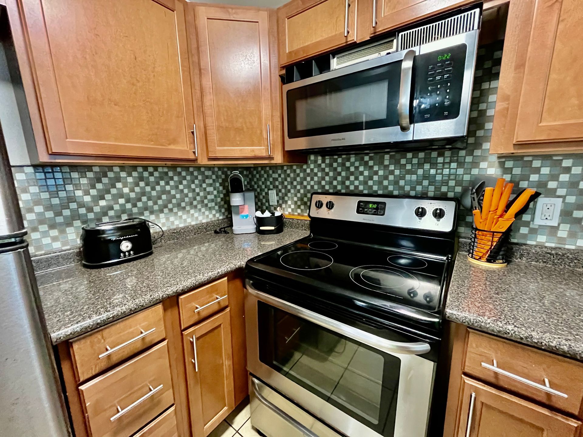 A fully equipped kitchen at Seabirds Motel at Kure Beach featuring granite countertops, a stove, microwave, and wooden cabinetry. This kitchen space is perfect for guests who prefer to prepare their own meals during their pet-friendly stay in North Carolina.
