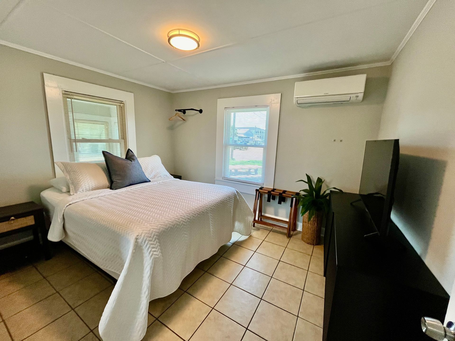 A modern guest room at Seabirds Motel at Kure Beach with a queen-sized bed, soft white bedding, and natural light from multiple windows. The room's minimalistic design provides a peaceful retreat, ideal for a pet-friendly stay in North Carolina.