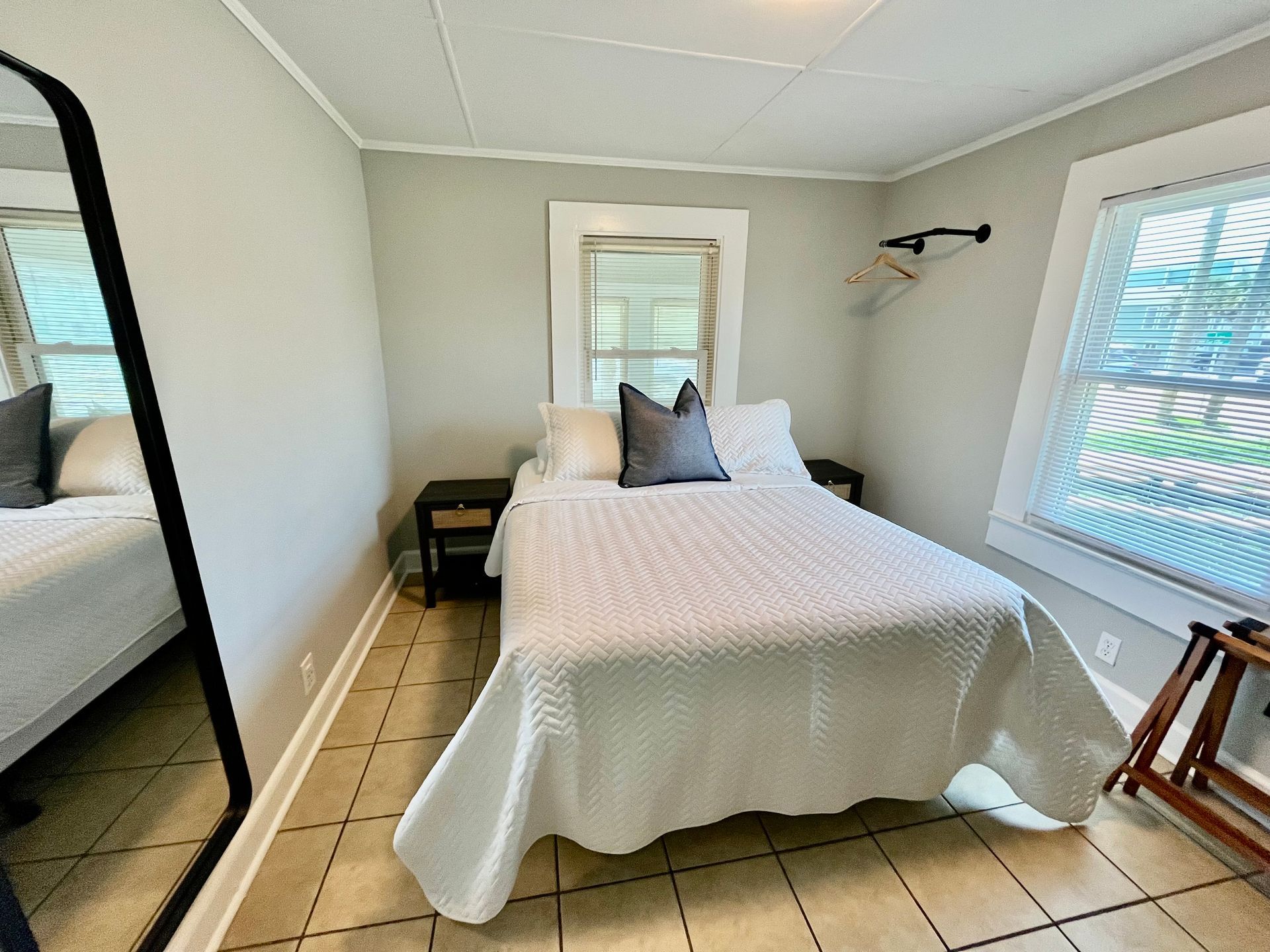 A cozy guest bedroom at Seabirds Motel at Kure Beach with a queen-sized bed, white bedding, and multiple windows providing natural light. This room offers a serene and comfortable setting, ideal for a pet-friendly stay in North Carolina.