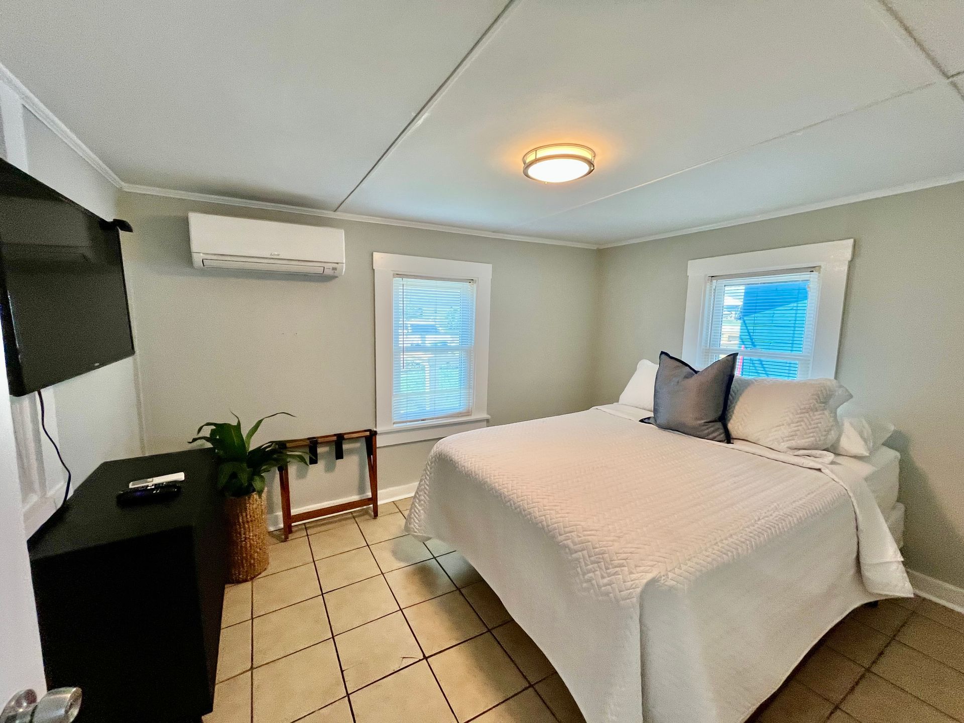 A bright and airy bedroom at Seabirds Motel at Kure Beach featuring a queen-sized bed with white linens, a flat-screen TV, and minimalist decor. The room offers a calm and comfortable environment for guests, perfect for a pet-friendly North Carolina lodging experience.