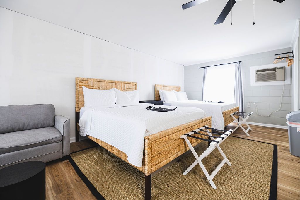 A well-appointed room at Seabirds Motel at Kure Beach featuring a queen-sized bed with a rattan frame, a sofa for additional seating, and a small dining area. This room offers a comfortable and versatile space for guests seeking a pet-friendly lodging option in North Carolina.