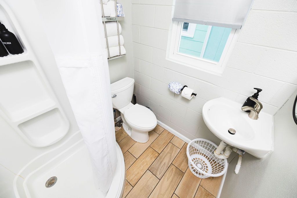 A clean and modern bathroom at Seabirds Motel at Kure Beach featuring a walk-in shower, toilet, and pedestal sink. The bright space offers all the necessary amenities for a comfortable and convenient pet-friendly stay in North Carolina.
