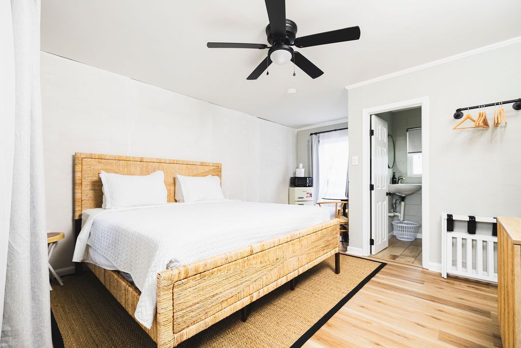 A bright guest room at Seabirds Motel at Kure Beach showcasing a queen-sized bed with white bedding, a ceiling fan, and minimalistic decor. The room provides a relaxing space for a pet-friendly North Carolina lodging experience.