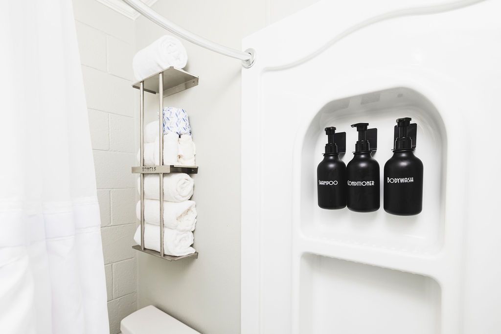 A bright and airy guest room at Seabirds Motel at Kure Beach featuring a queen-sized bed with a rattan headboard, white linens, and a hanging clothes rack. This room offers a comfortable setting for a pet-friendly stay in North Carolina.