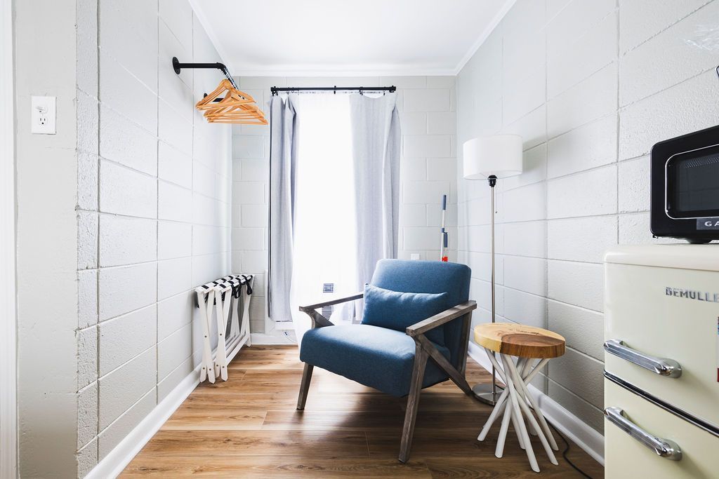 A cozy corner room at Seabirds Motel at Kure Beach featuring a comfortable blue armchair, side table, and retro mini-fridge with a microwave. The room is designed for relaxation and convenience, offering a comfortable stay at this pet-friendly North Carolina lodging.