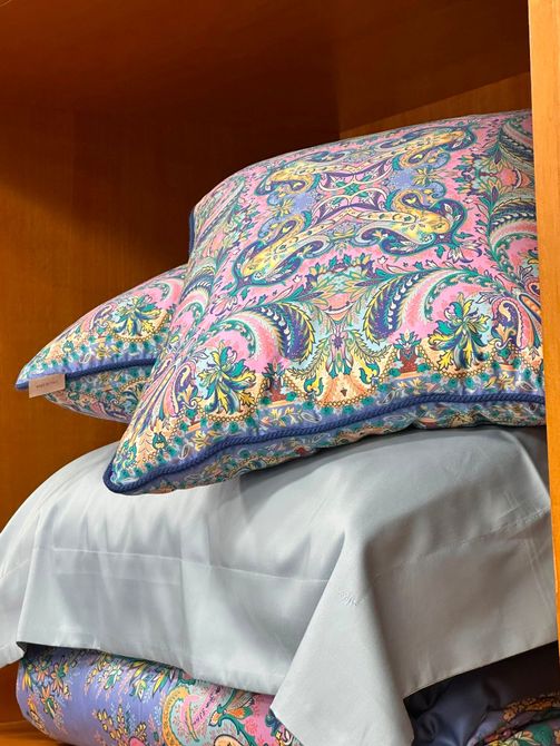 Cuscini colorati e decorati impilati su un letto bianco o su uno scaffale all'interno di un mobile di legno.