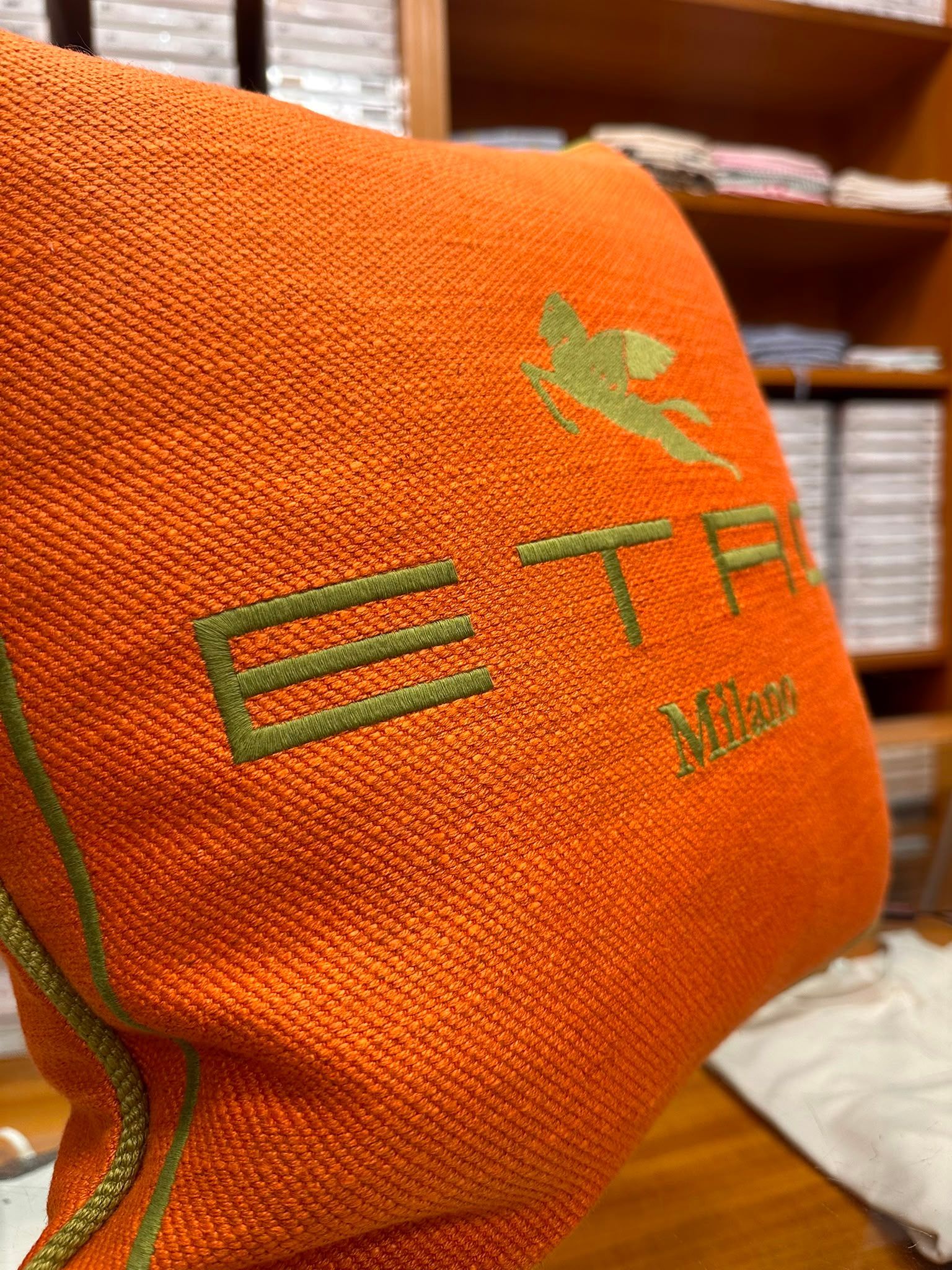 Primo piano di una borsa arancione testurizzata con logo e testo ricamati in verde.