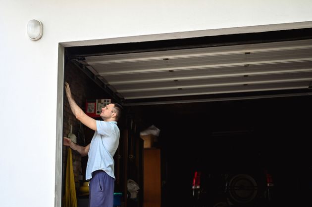 A man is standing in a garage opening a garage door.