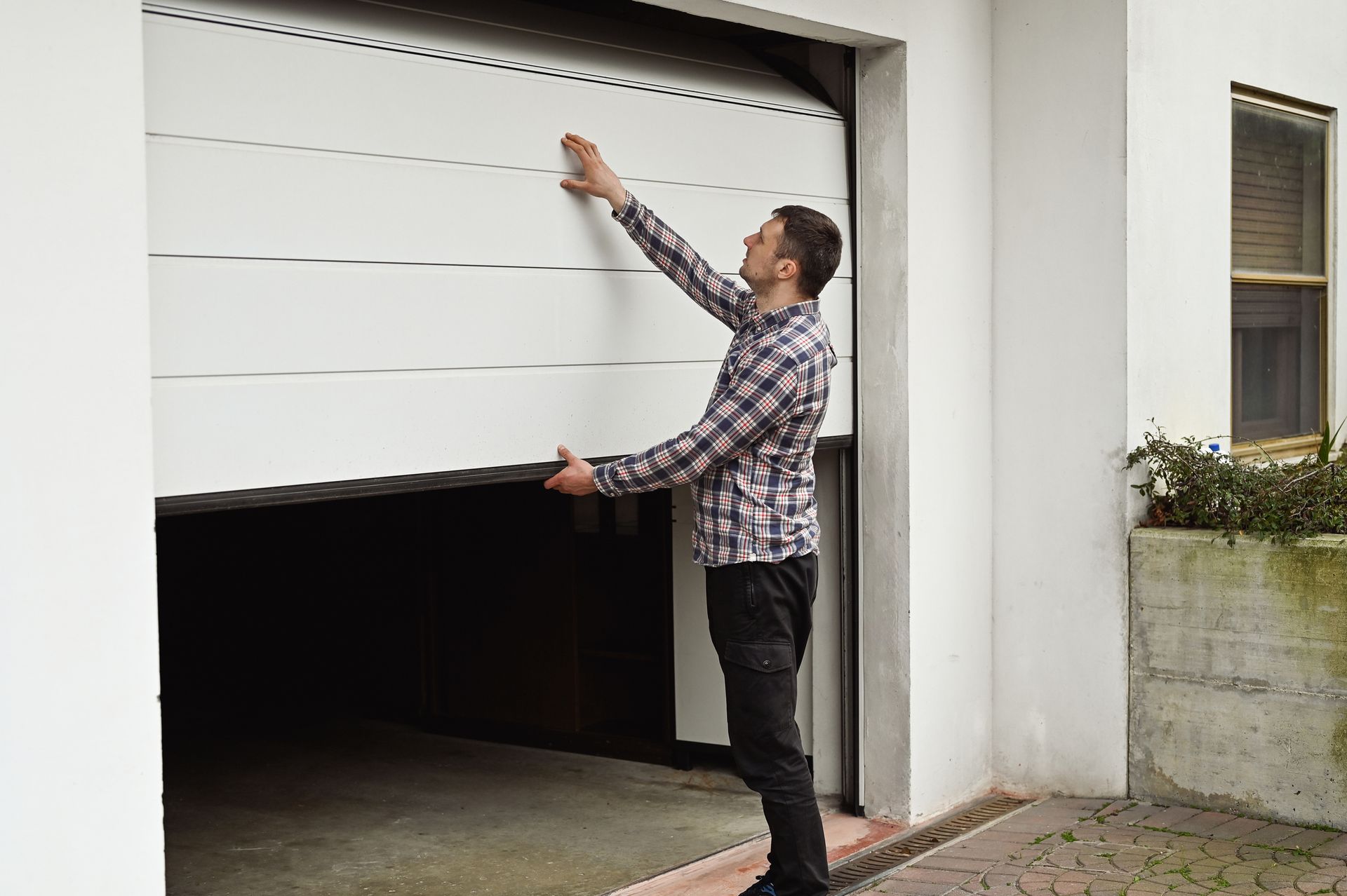 A man in a plaid shirt is opening a garage door.