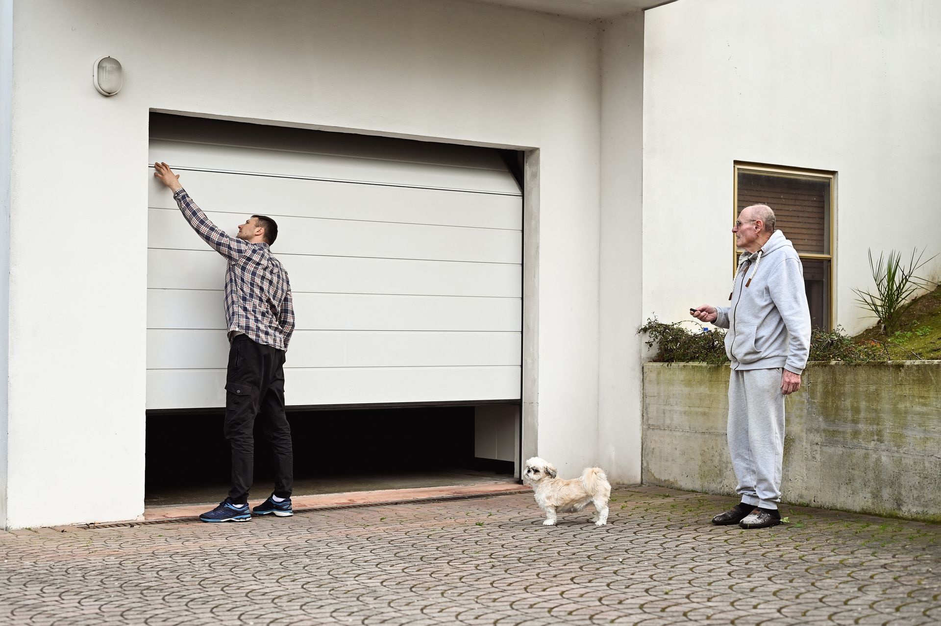 Two men and a dog are standing in front of a garage door.