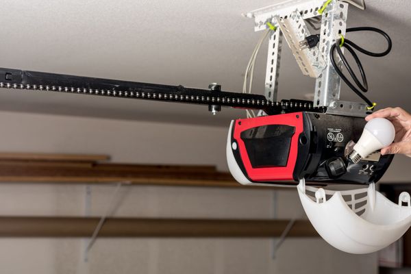 A person is holding a light bulb next to a garage door opener.