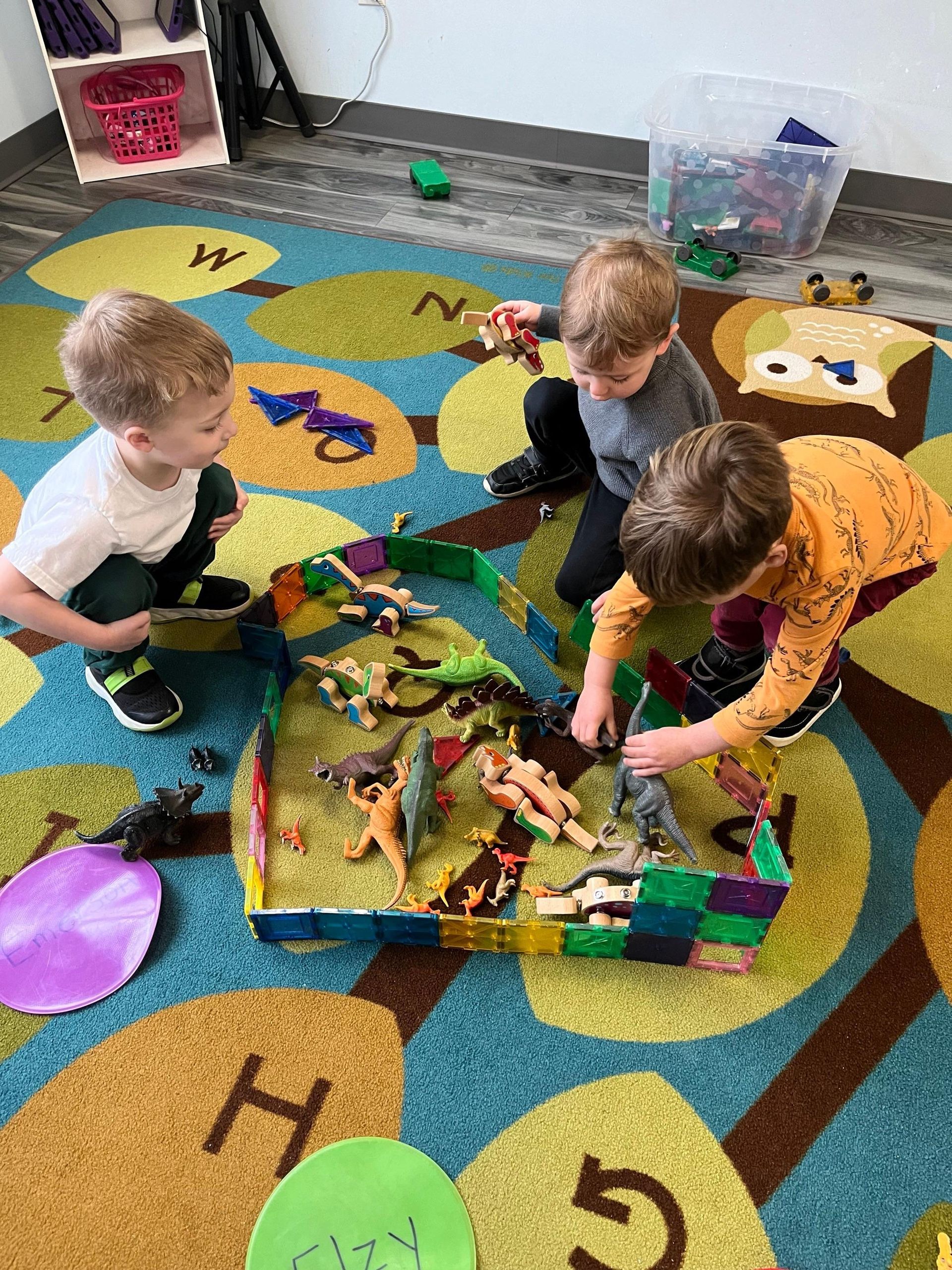 Three young boys are playing with toy dinosaurs on a rug.