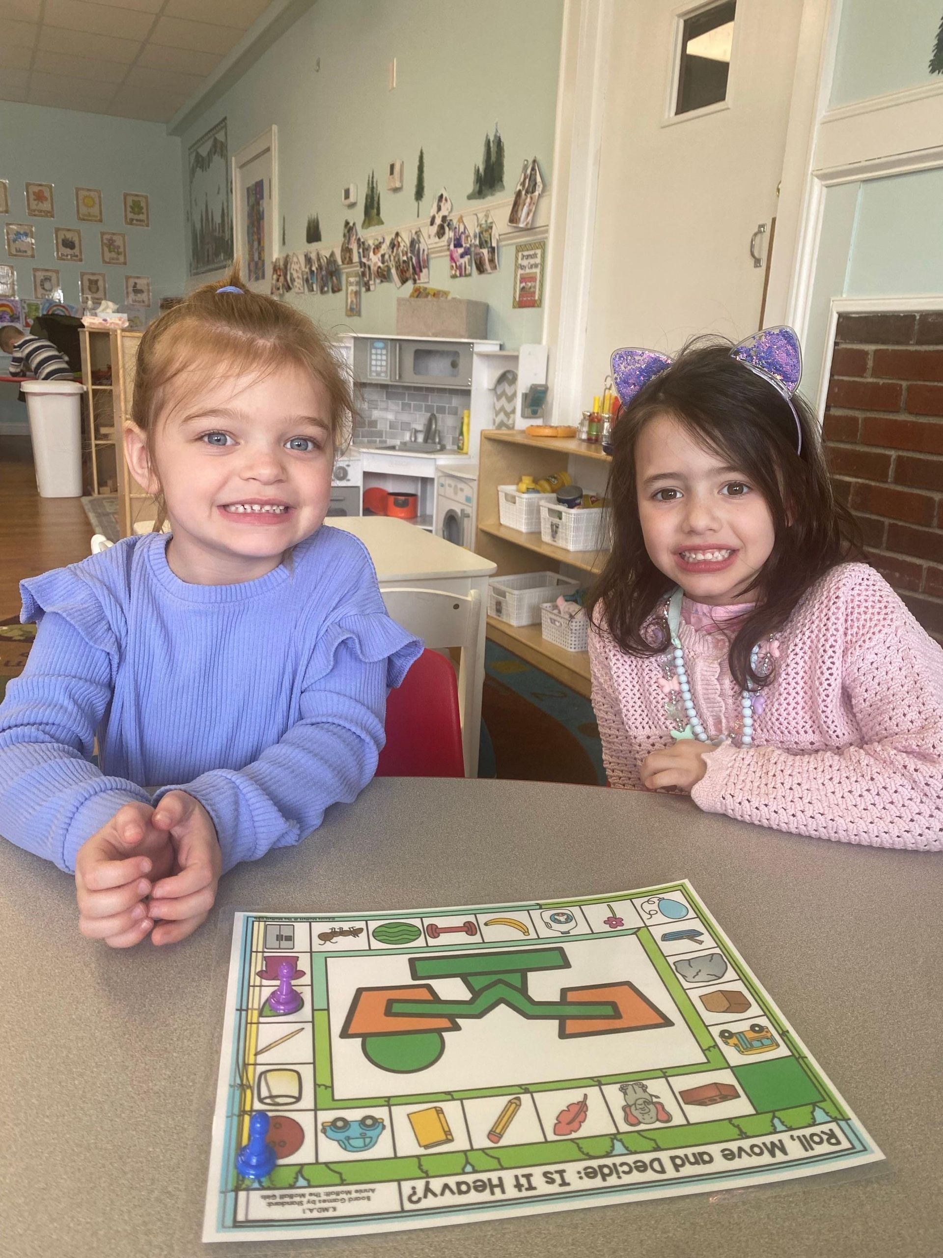 Two little girls are sitting at a table with a board game on it.