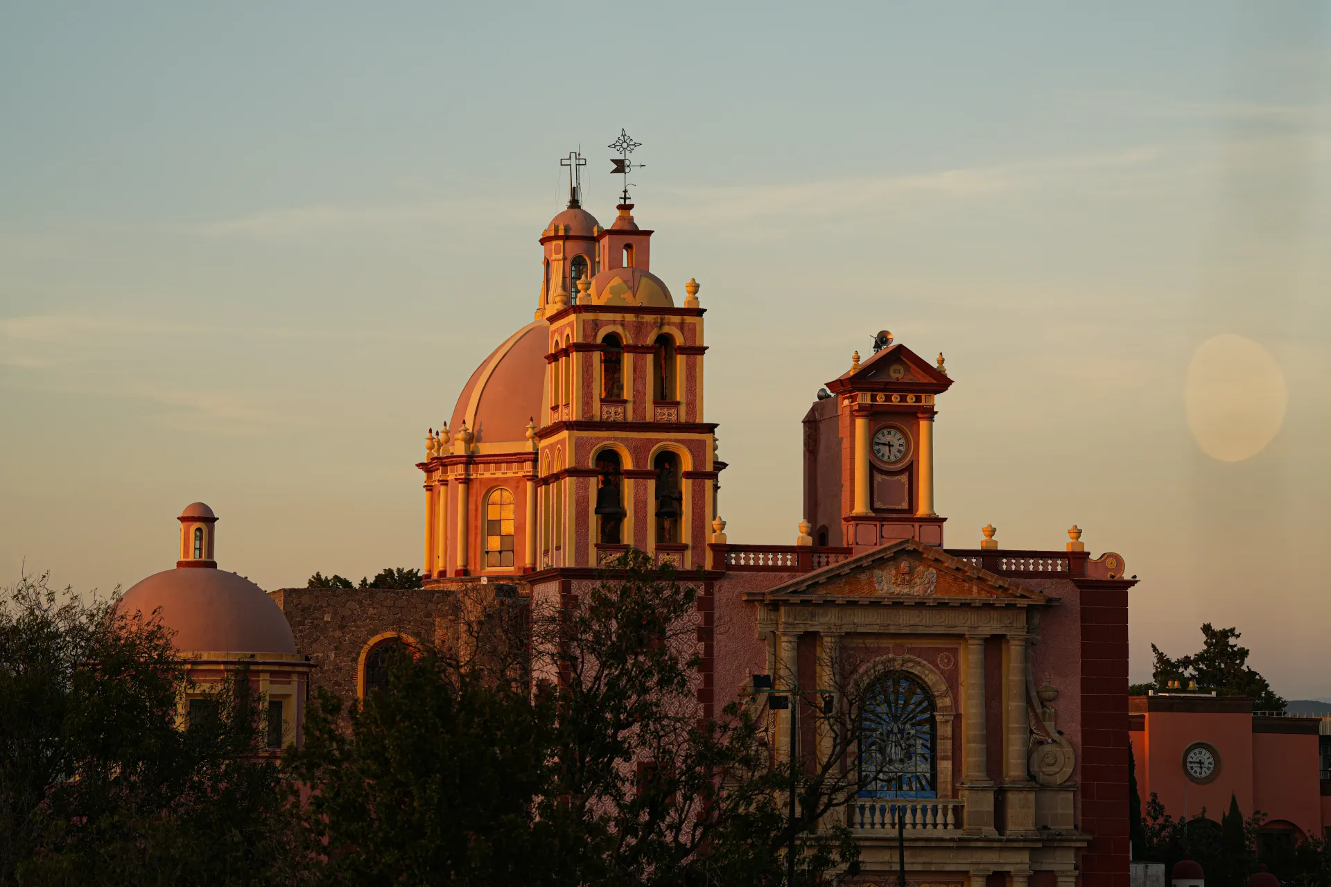 Iglesia histórica iluminada por la puesta de sol, con sus cúpulas y campanario recortados contra un cielo despejado.