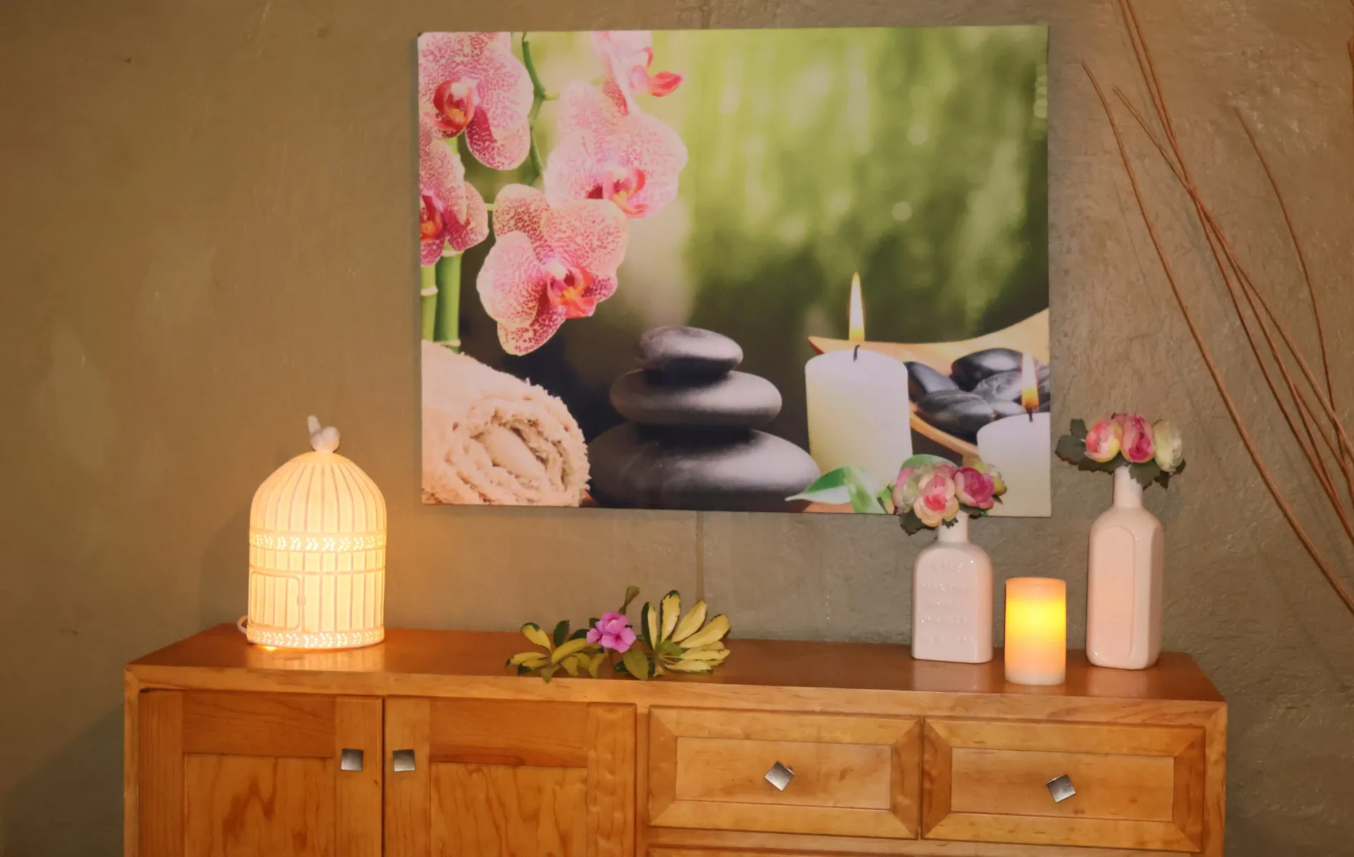 Wooden dresser with candles and pink flowers beneath a spa stones wall art print