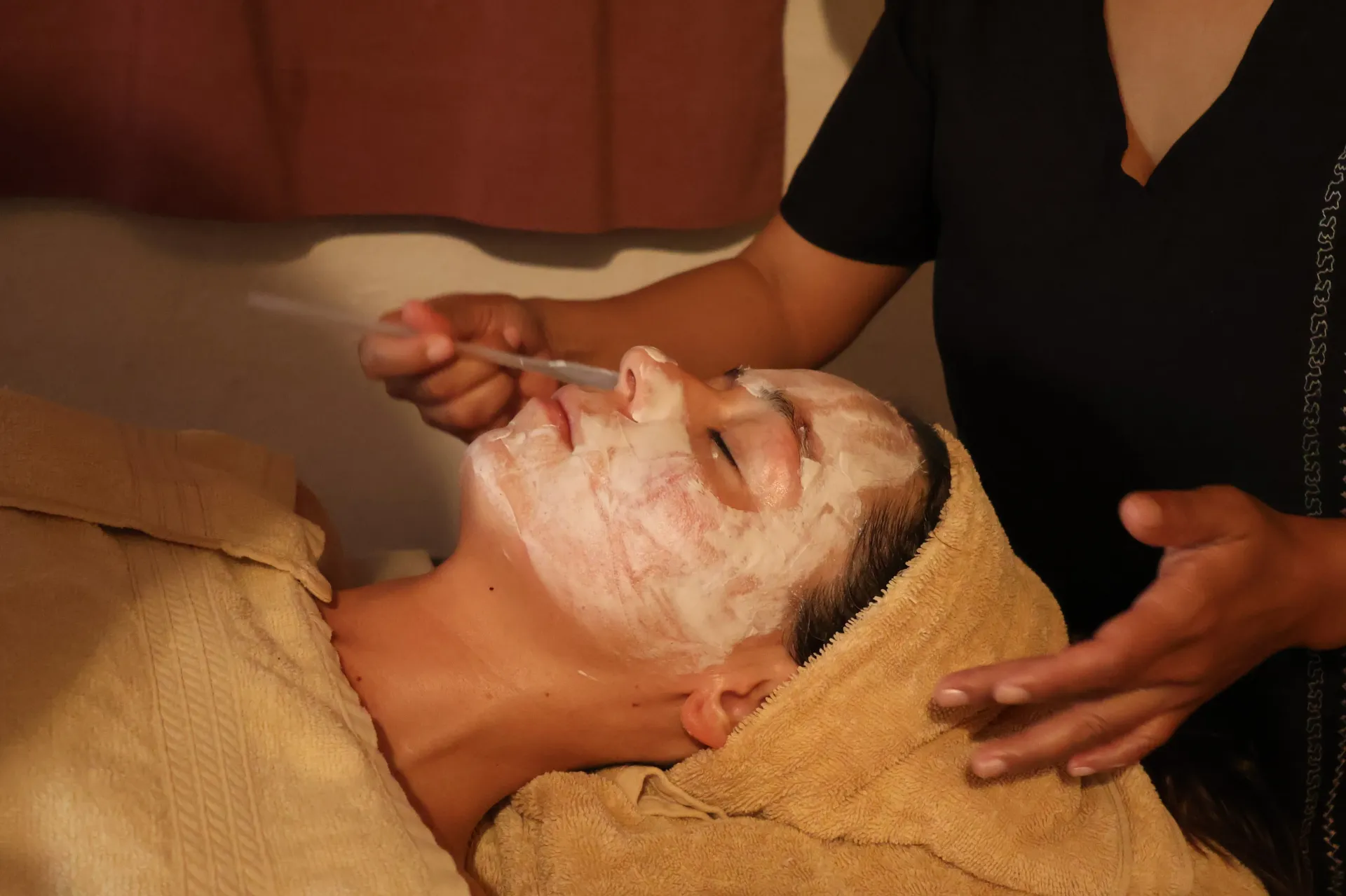 Person receiving a facial treatment with cream applied while lying on a towel-covered spa bed
