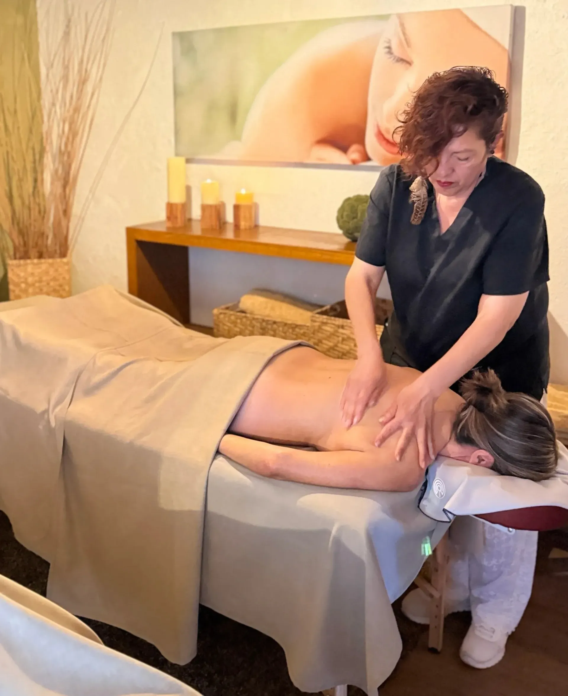 Massage therapist giving a back massage in a spa room with candles and a folded towel