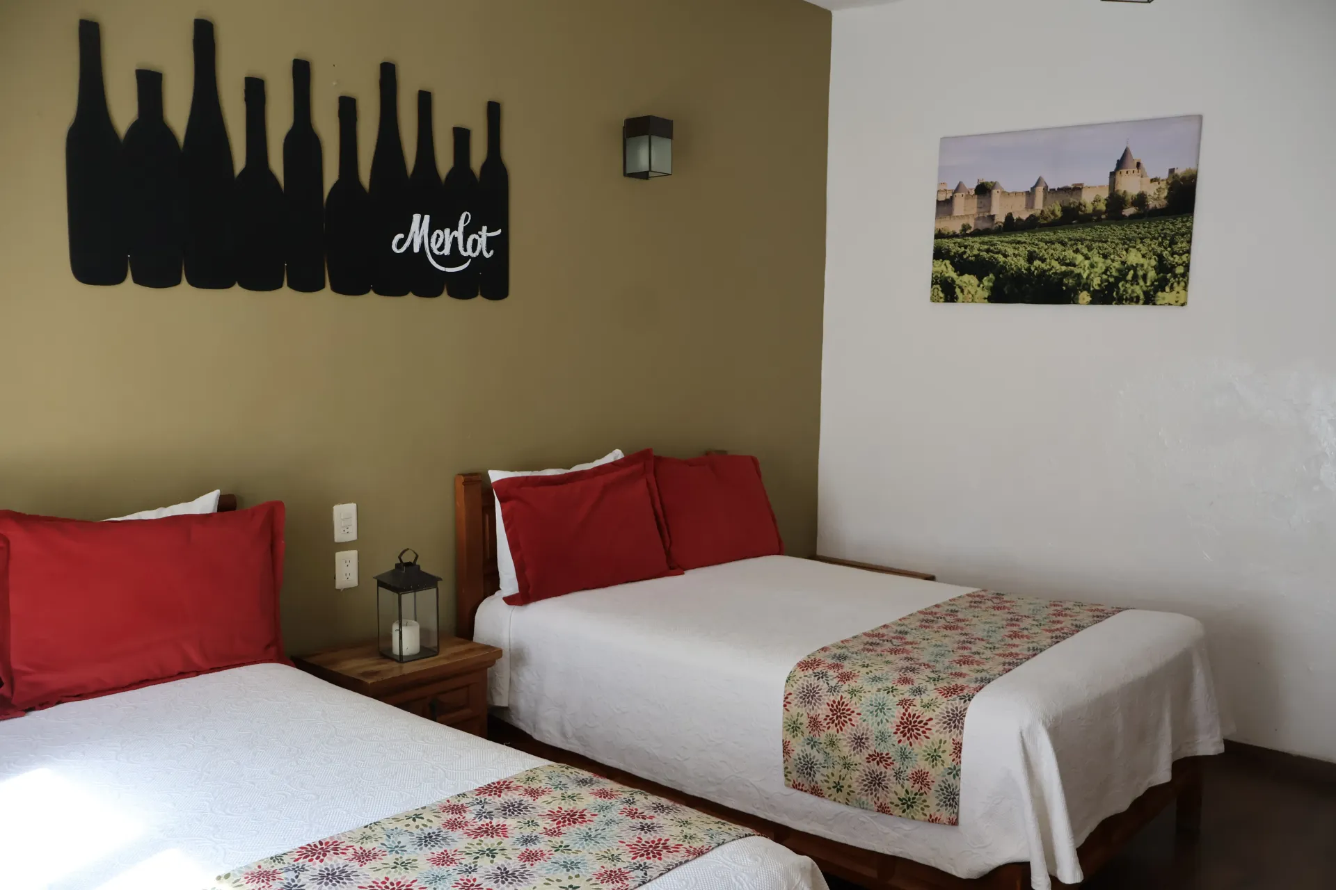 Dos camas individuales con almohadas rojas en una habitación de invitados de color beige, con cuadros en la pared.