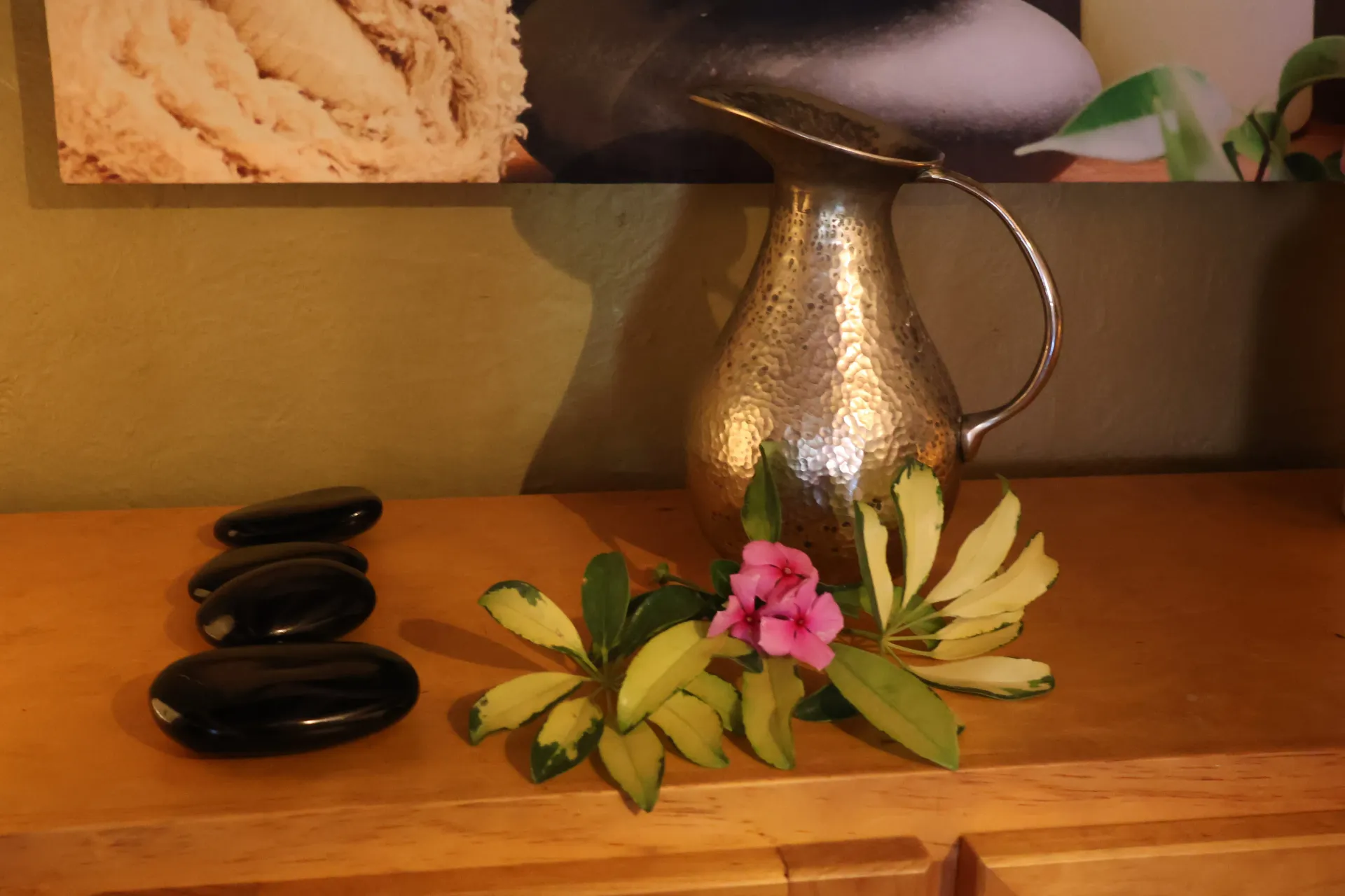 Decorative silver pitcher with stones and flowers on a wooden table against a warm wall