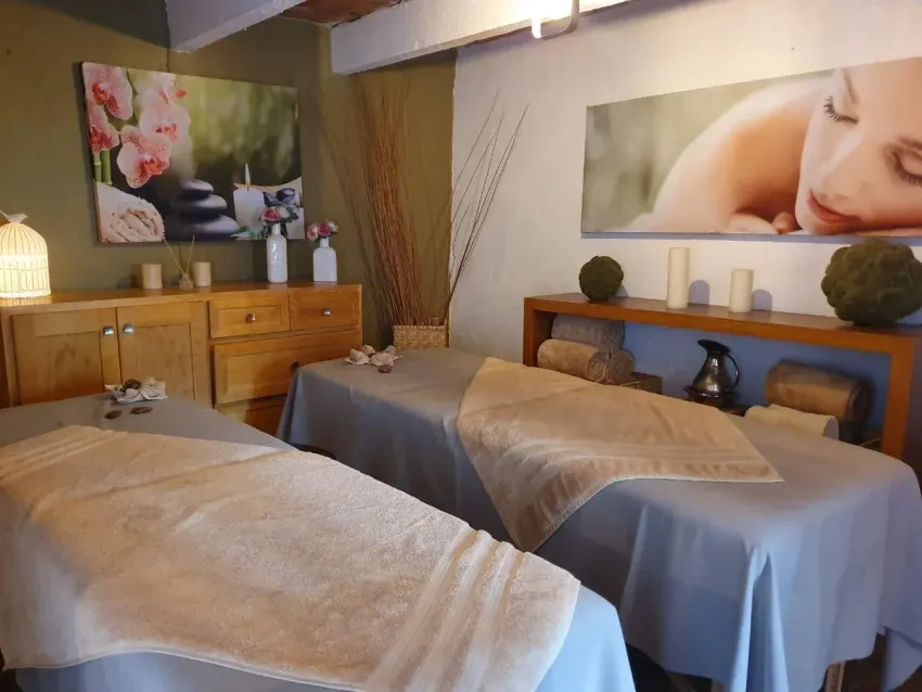 Sala de masajes con dos camillas de tratamiento, armarios de madera y decoración de spa que incluye flores y velas.