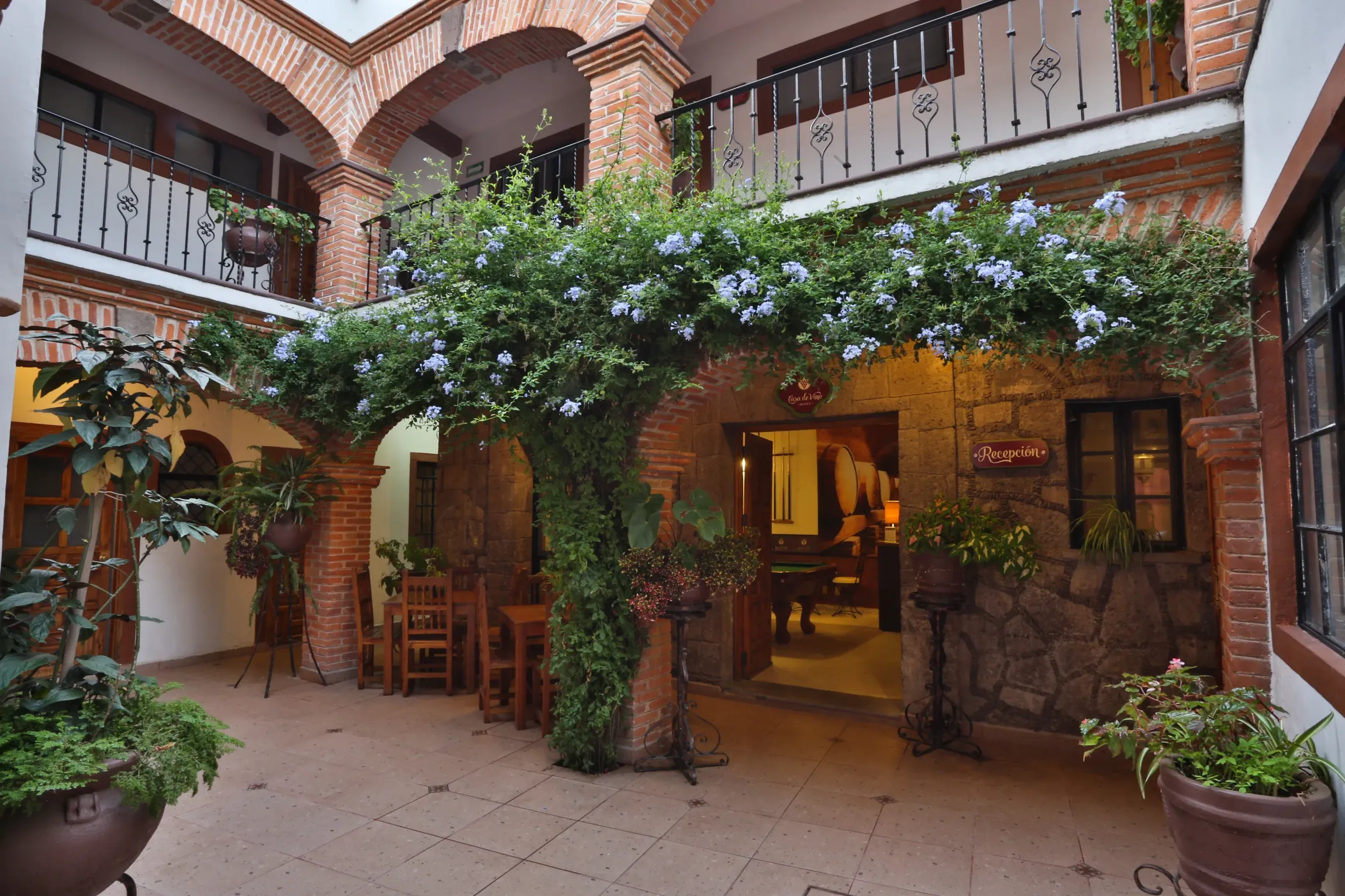 Restaurante con patio interior, arcos cubiertos de enredaderas, paredes de ladrillo y mesas de madera bajo una iluminación.
