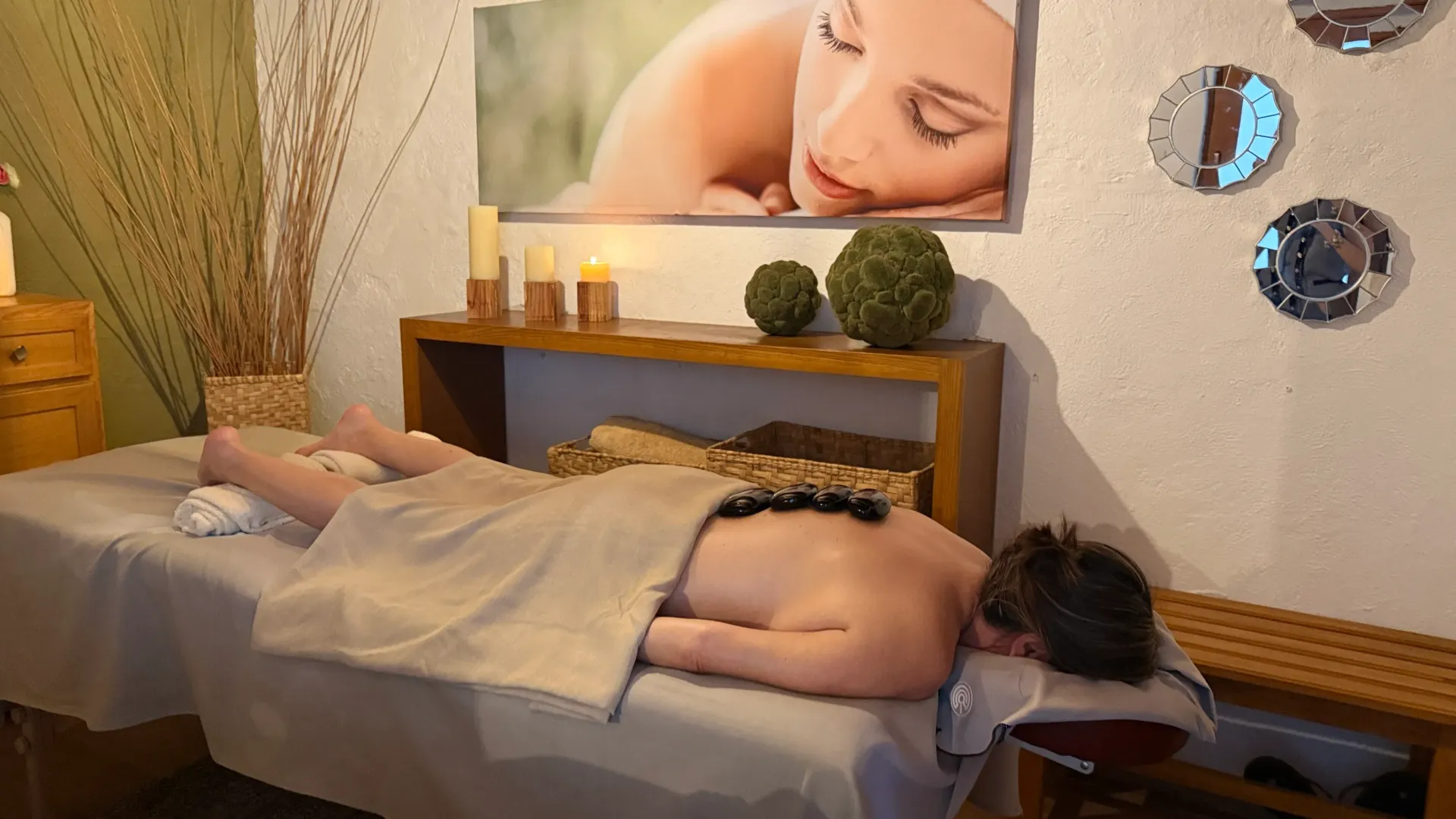 Massage table in a spa room with a person lying face down and candles on a shelf above them