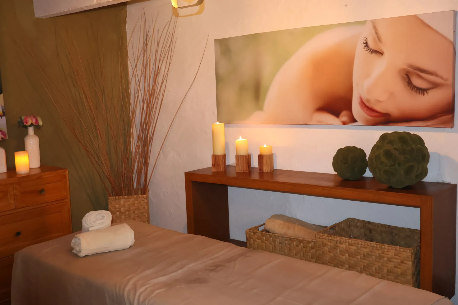 Spa room with massage table, candles, rolled towels, and a wall photo of a woman resting
