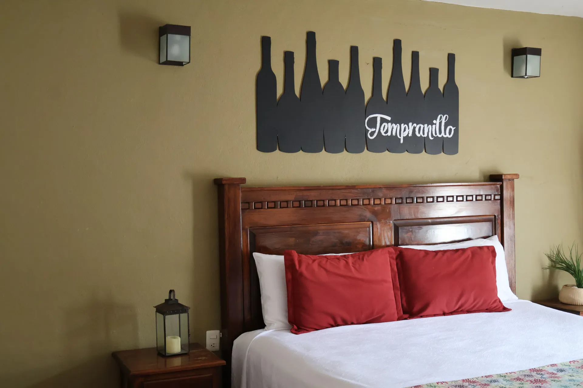 Habitación acogedora con cabecero de madera, almohadas rojas, ropa de cama blanca y un cuadro en la pared encima de la cama.