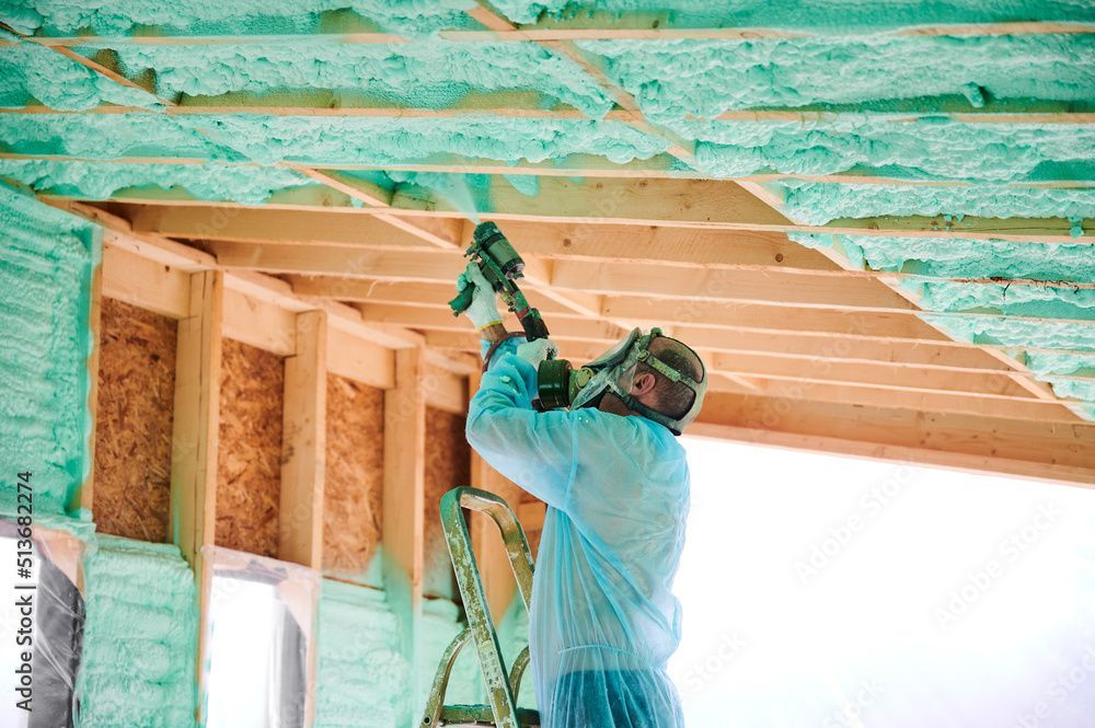 Man spraying insulation foam, wearing protective gear, inside a wooden framed building. Man spraying insulation foam, wearing protective gear, inside a wooden framed building.